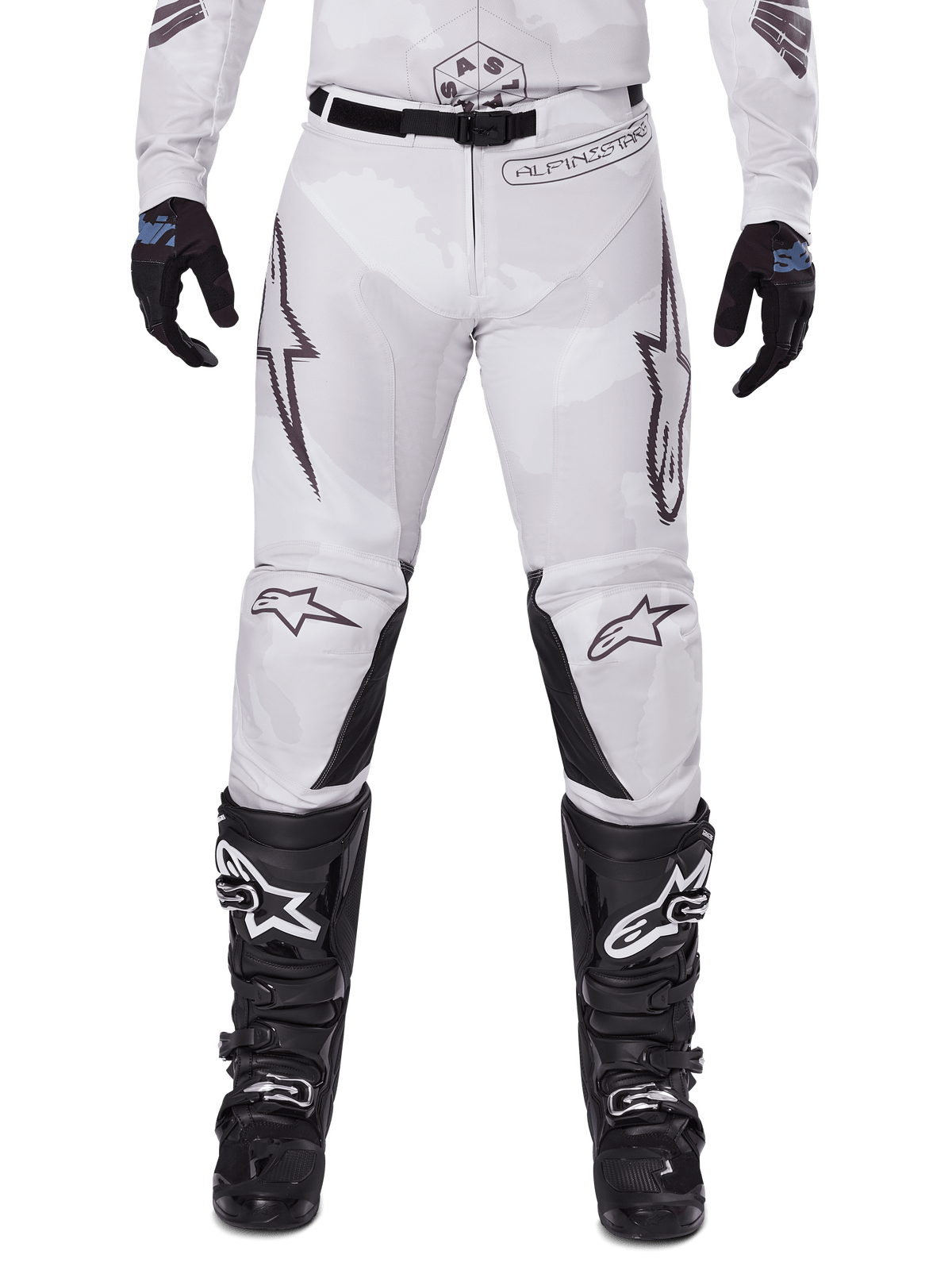 Alpinestars 2025 Racer Hollow Hose, Motocross-Hose, Light Camo Brown, getragen mit schwarzen Handschuhen und Motocross-Stiefeln, mit dezentem Camouflage-Muster, schwarzen Grafikdrucken und Astars-Logos, ergonomisches Design für Performance-Offroad-Fahrten
