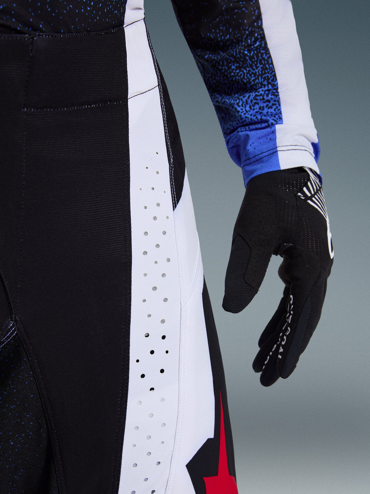 Alpinestars 2026 Techstar Knif Pants, Motocross Pants, Black White and Red, close-up highlighting laser-cut perforations on side panels and red star branding, paired with a matching jersey and black motocross glove.