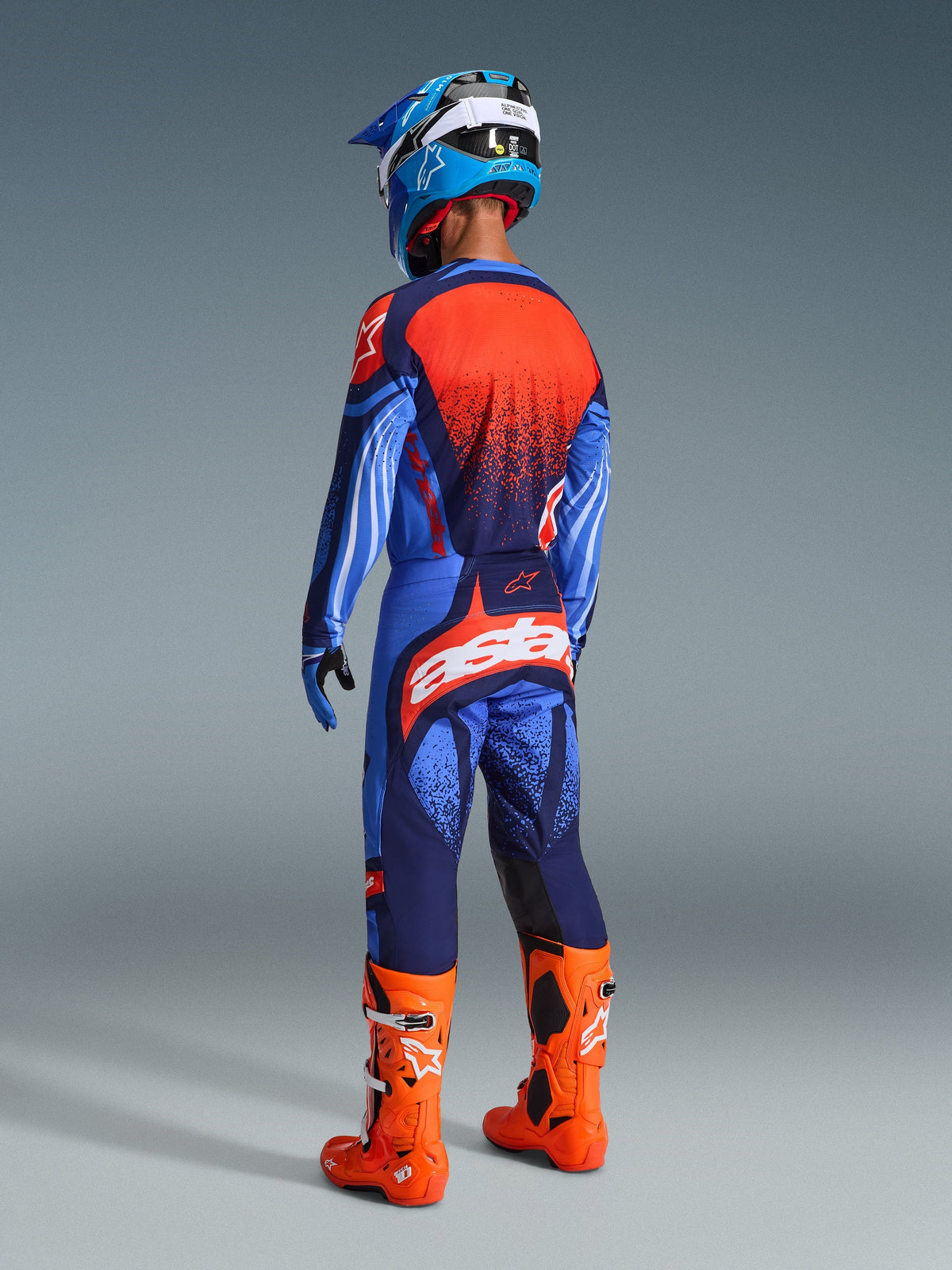 Alpinestars 2026 Techstar Nomur Pants, Motocross Pants, Dark Navy, Orange and UCLA Blue, back view of rider in complete gear, large white branding on the seat, bright orange boots, blue jersey and helmet, professional motocross racing outfit.