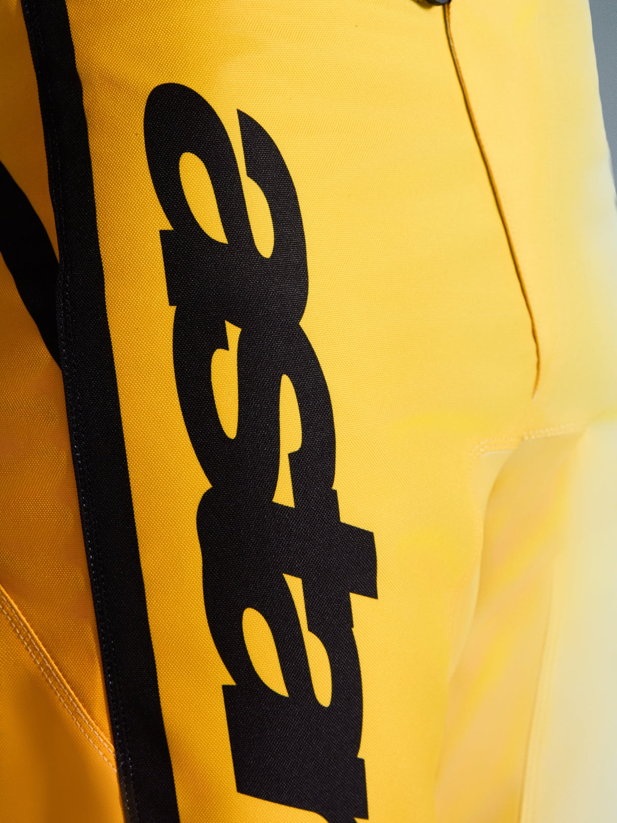 Nahaufnahme der Alpinestars 2026 Fluid Apex Hose, Motocross-Hose, Gelb und Schwarz, mit einem großen vertikalen schwarzen Logo, texturiertem, strapazierfähigem Material und ergonomischen Details für Offroad-Performance