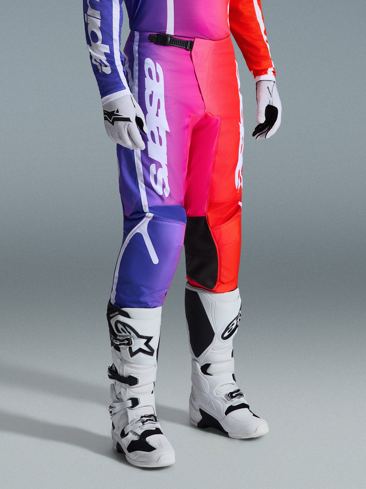 Alpinestars 2026 Fluid Apex Pants, Motocross Pants, Multicolor purple, pink, and red gradient, worn with white and black motocross boots and gloves, featuring white vertical branding and black knee accents, performance off-road gear