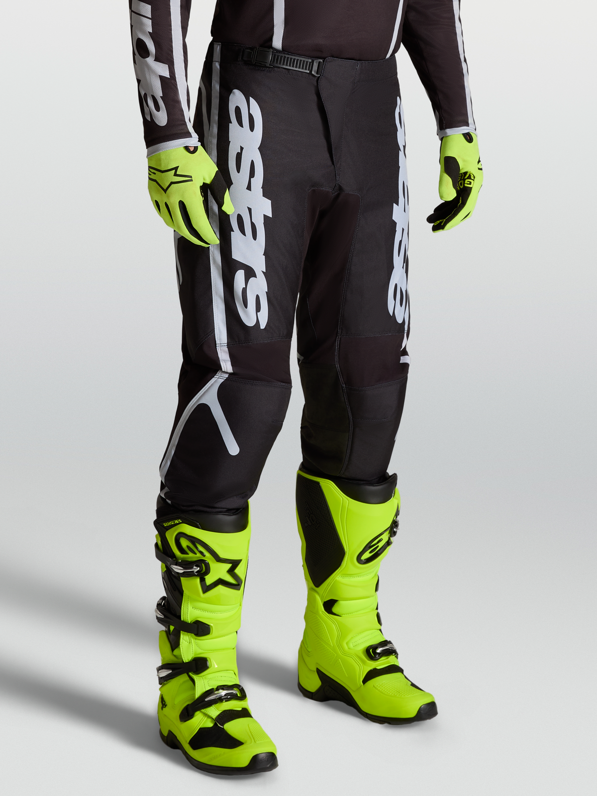 Alpinestars Fluid Apex V2 Hose, Motocross-Ausrüstung für Herren, Schwarz und Silber, mit 600D-Polygewebe, getragen mit neongelben Stiefeln.