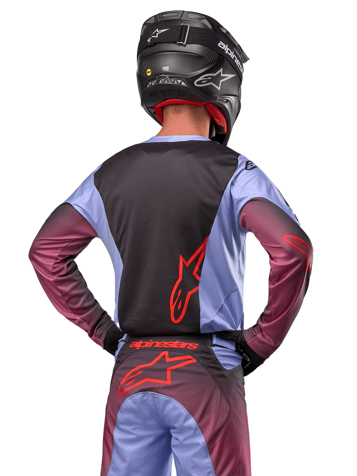 Motocross-Fahrer von hinten, trägt Alpinestars 2024 Racer Hoen Ausrüstung, Trikot in Lavan Purple und Schwarz mit rotem Logo, passende Hose mit roten Akzenten, schwarzer Helm, abgestimmtes Outfit für Offroad-Rennen