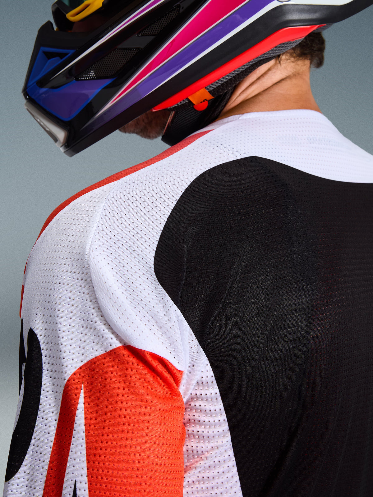 Alpinestars 2026 Racer Air Portl Trikot, Motocross-Trikot, mehrfarbig mit weißen, schwarzen und roten Einsätzen, Nahaufnahme der perforierten Mesh-Konstruktion an Schulter und Rücken zur Belüftung, getragen mit einem farbenfrohen Motocross-Helm