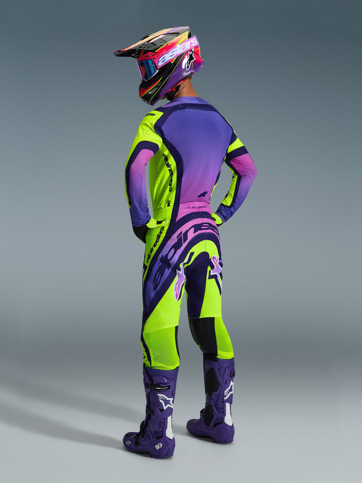 Motocross-Fahrer in kompletter Rennausrüstung, Rückansicht, 2026 Supertech Vista Jersey in Gelb, Lila und Schwarz, passende Hose mit markantem Branding, lila Helm mit pinker Brille und lila Stiefel mit weißen Logos, professionell abgestimmtes Motocross-Outfit.