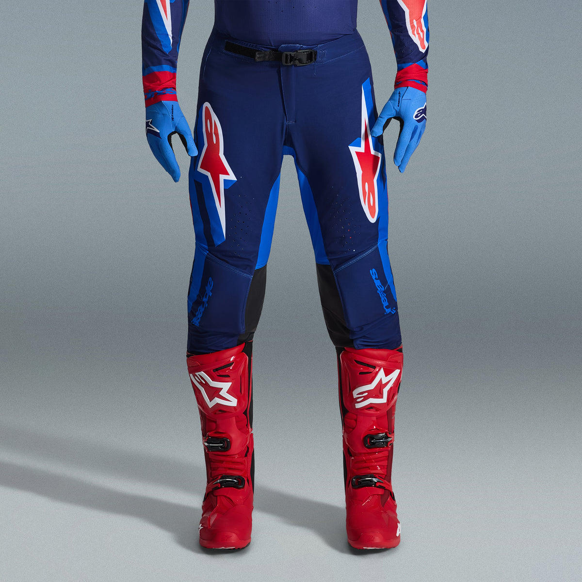 Alpinestars 2026 Supertech Vista Gear Set, Motocross pants in navy and bright blue with red and white logos, paired with light blue gloves and bright red motocross boots, professional racing apparel.