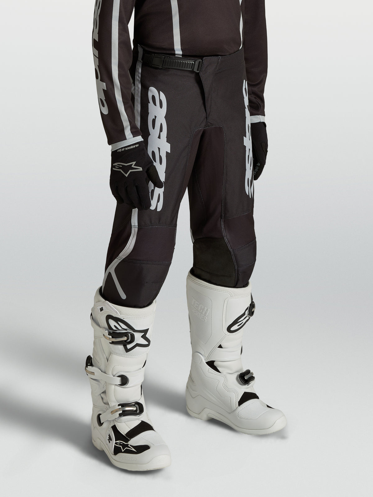 Alpinestars Jugend Fluid Apex V2 Hose, Motocross-Hose für junge Fahrer in Schwarz und Silber, ergonomisch vorgeformte Passform, getragen mit weißen Tech-Stiefeln.