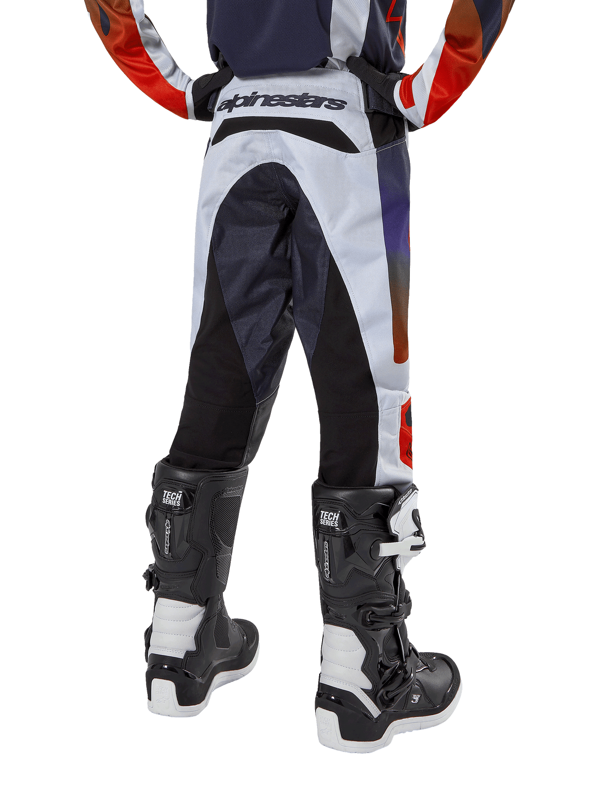 Alpinestars Jugend 2024 Racer Hoen Hose, Motocross-Hose, Hellgrau mit Akzenten in Hot Orange und Schwarz, Rückansicht mit schwarzen Einsätzen an Gesäß und Beinen, markantes Branding am hinteren Bund, getragen mit schwarz-weißen Motocross-Stiefeln für Offroad-Rennen