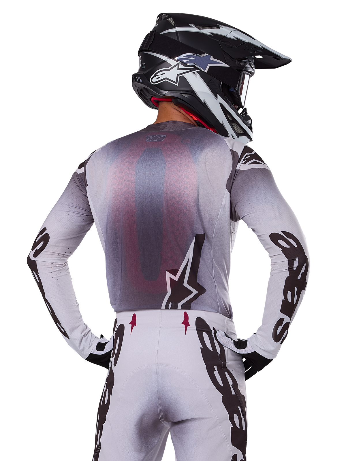 Motocross-Fahrer von hinten im Alpinestars 2025 Supertech Maker Trikot, Silber und Schwarz mit rotem Mesh-Rückeneinsatz und schwarzen Ärmellogos, kombiniert mit passender Motocross-Hose und einem schwarz-weißen Helm, professionelle Offroad-Rennausrüstung