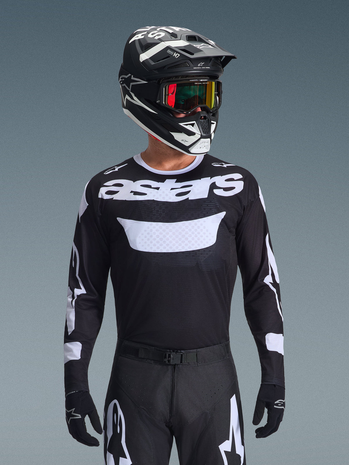 Motocross-Fahrer im Alpinestars 2026 Racer Air Riway Gear Set, schwarzes Jersey mit weißem „astars“-Logo und belüftetem Brustbereich, schwarze Hose mit weißen Akzenten, passender schwarz-weißer Helm mit irisierender Brille, schwarze Handschuhe, Hochleistungs-Motocross-Ausrüstung in Schwarz und Weiß.