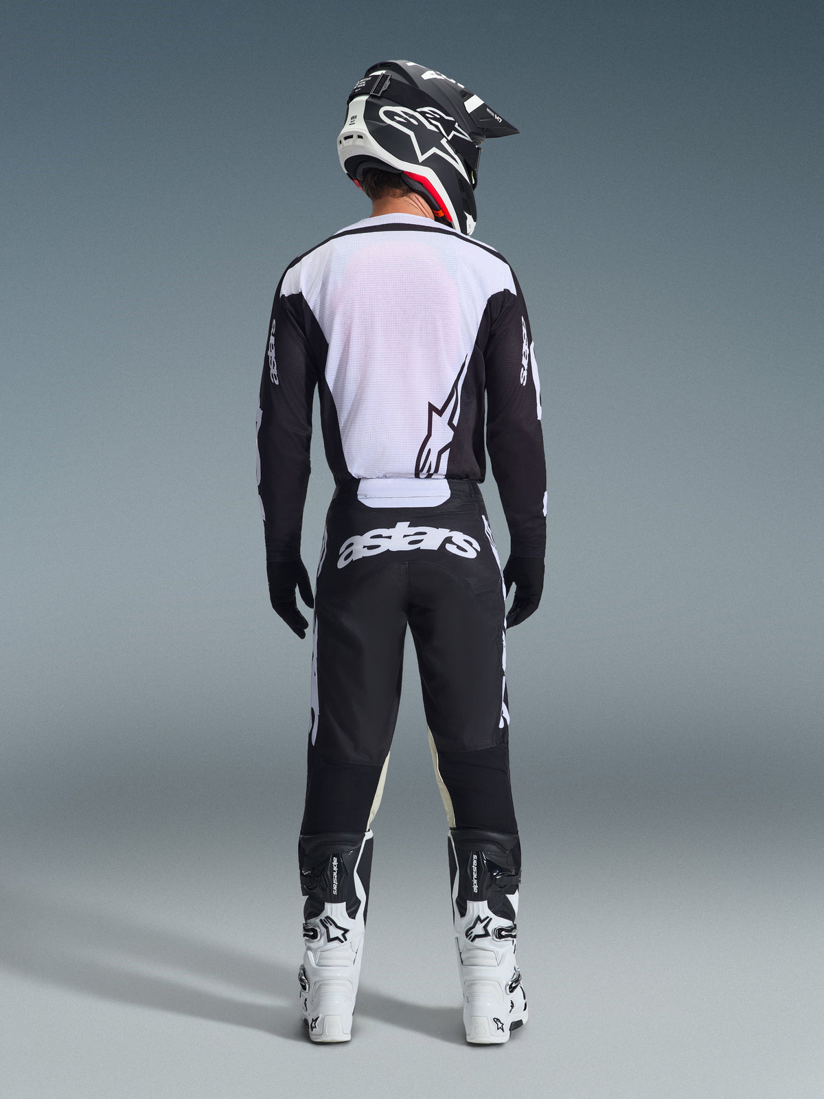 Rear view of a motocross rider wearing the 2026 Racer Air Riway Jersey in Black and White, featuring a breathable mesh back panel, paired with matching black motocross pants with white 'astars' branding, a black and white helmet, and white racing boots.