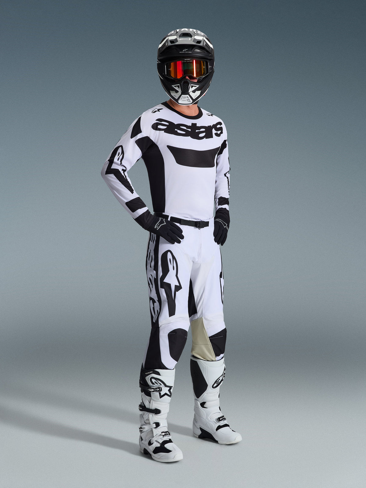 Alpinestars 2026 Racer Riway Gear Set, Motocross-Fahrer in weiß-schwarzer Rennbekleidung, weißes Jersey mit schwarzem „astars“-Logo auf der Brust, weiße Hose mit schwarzen Akzenten, schwarzer Helm mit oranger Goggles, weiße Stiefel, abgestimmte Ausrüstung für Motocross und Offroad-Fahren