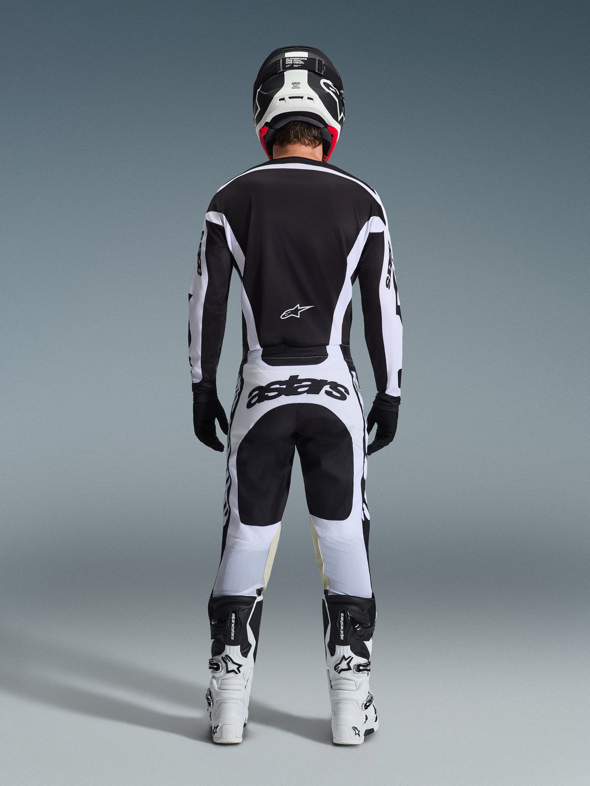 Rückansicht eines Motocross-Fahrers im 2026 Racer Riway Gear Set in Schwarz und Weiß, bestehend aus einem schwarzen Jersey mit weißen Akzenten, einer weißen Hose mit markantem „astars“-Branding am Gesäß, schwarzem Helm, weißen Stiefeln und schwarzen Handschuhen, komplettes professionelles Offroad-Rennoutfit.