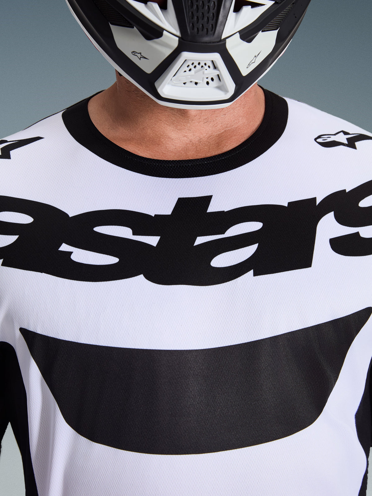 Alpinestars 2026 Racer Riway Trikot, Motocross-Trikot, Weiß und Schwarz, Nahaufnahme der Brust mit markantem schwarzem Astars-Logo und schwarzem Kragen, getragen mit weiß-schwarzem Helm, Performance-Offroad-Ausrüstung