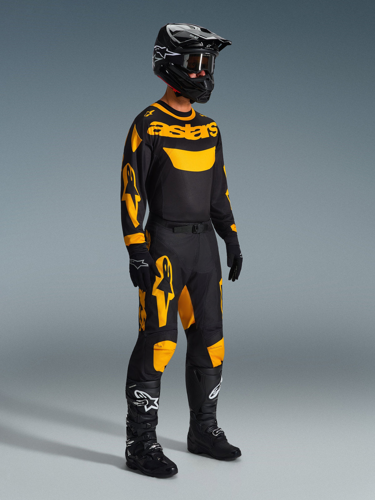 Motocross-Fahrer in kompletter Rennausrüstung, Alpinestars 2026 Racer Riway Trikot in Gelb und Schwarz, passende schwarz-gelbe Hose, schwarzer Helm mit Brille, schwarze Stiefel und Handschuhe, abgestimmtes Outfit für Offroad-Rennen