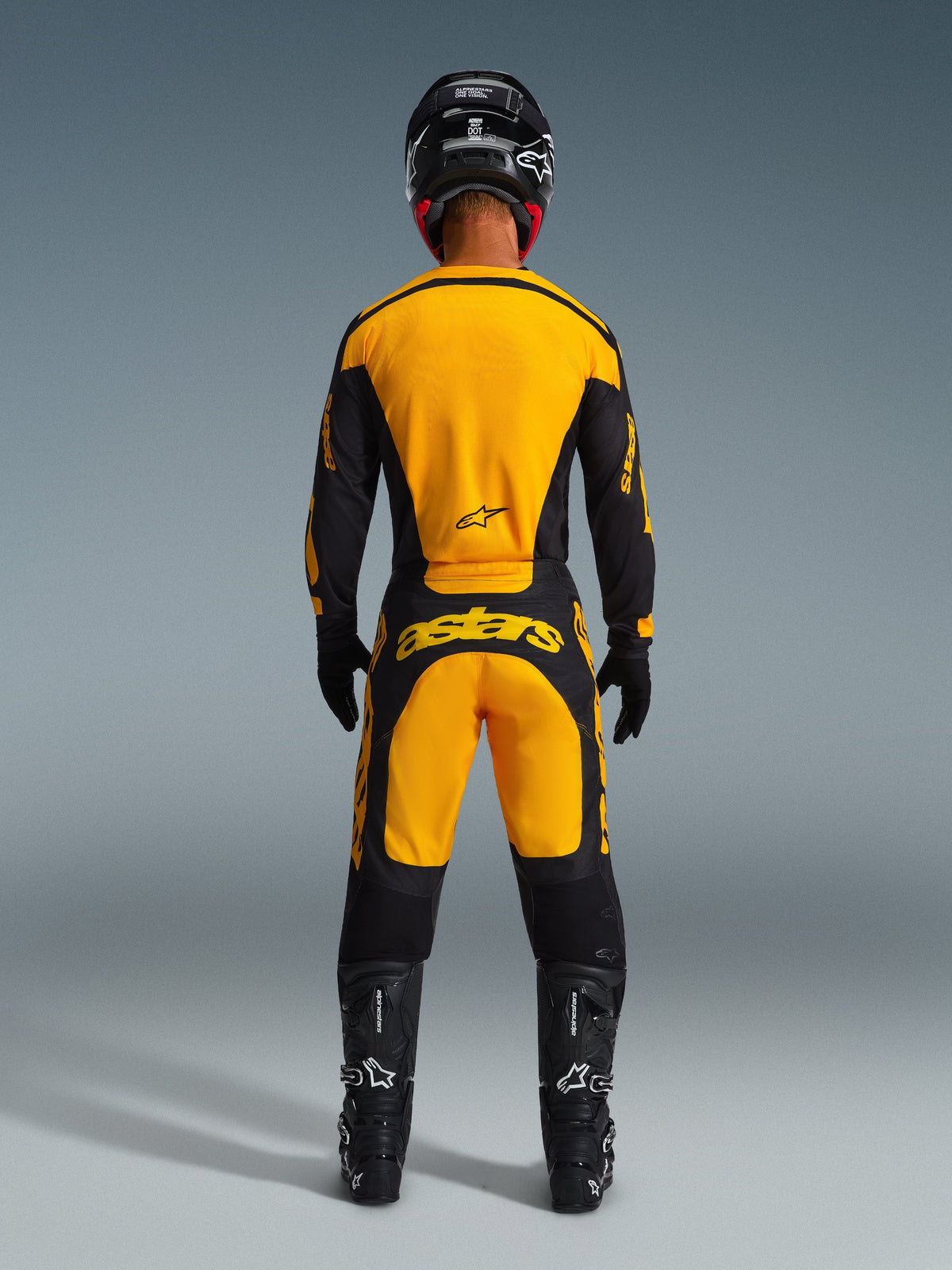 Motocross-Fahrer von hinten im Alpinestars 2026 Racer Riway Gear Set, Trikot und Hose in Gelb und Schwarz, mit „astars“-Branding auf der Rückseite, kombiniert mit schwarzem Helm, Handschuhen und Stiefeln, komplette Offroad-Rennausrüstung.