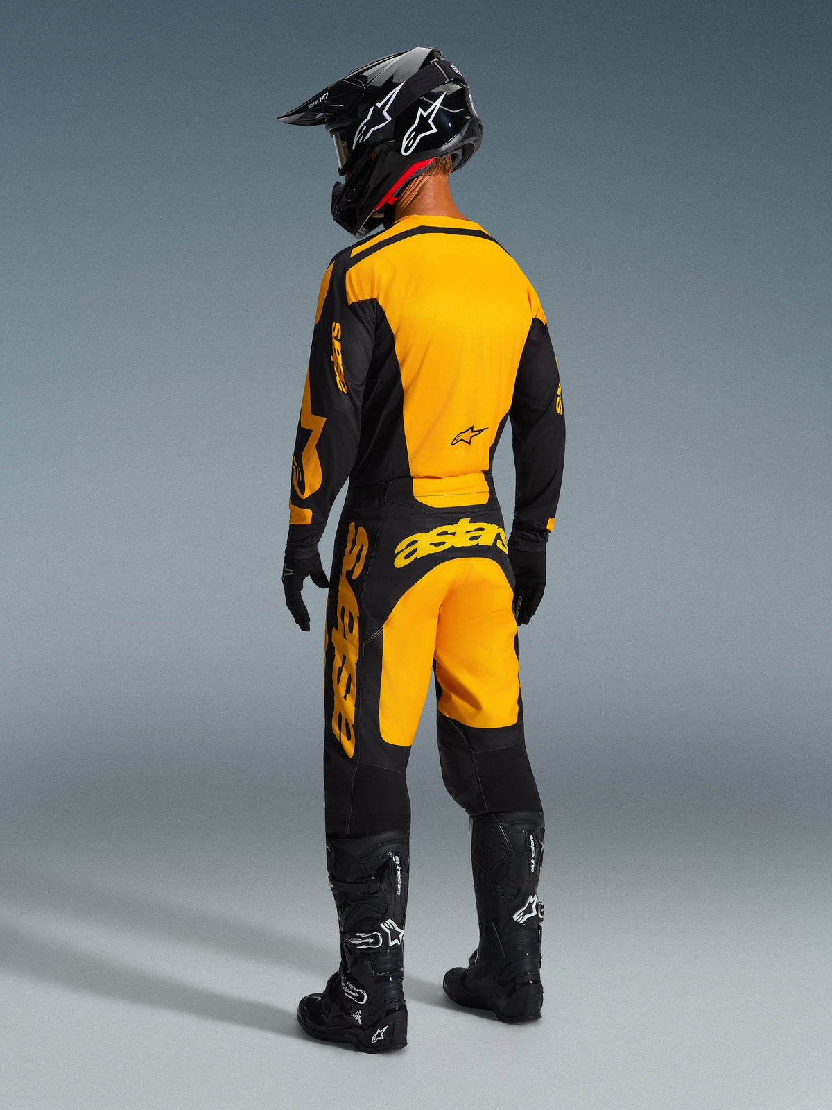 Motocross rider wearing complete racing gear, Alpinestars 2026 Racer Riway Jersey in Yellow and Black, matching yellow and black pants, black helmet, black gloves, and black boots, rear view of coordinated off-road outfit