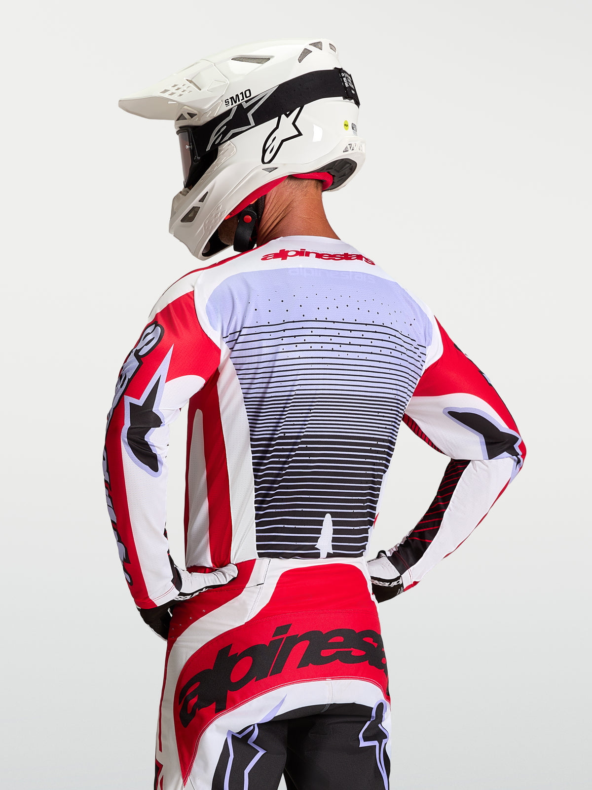 Alpinestars Techstar Maven Trikot, Motocross-Rennsport-Trikot für Herren, Rot und Weiß, Rückansicht eines Fahrers mit Motocross-Helm, atmungsaktives Material mit lasergeschnittener Belüftung und athletischer Rennpassform.