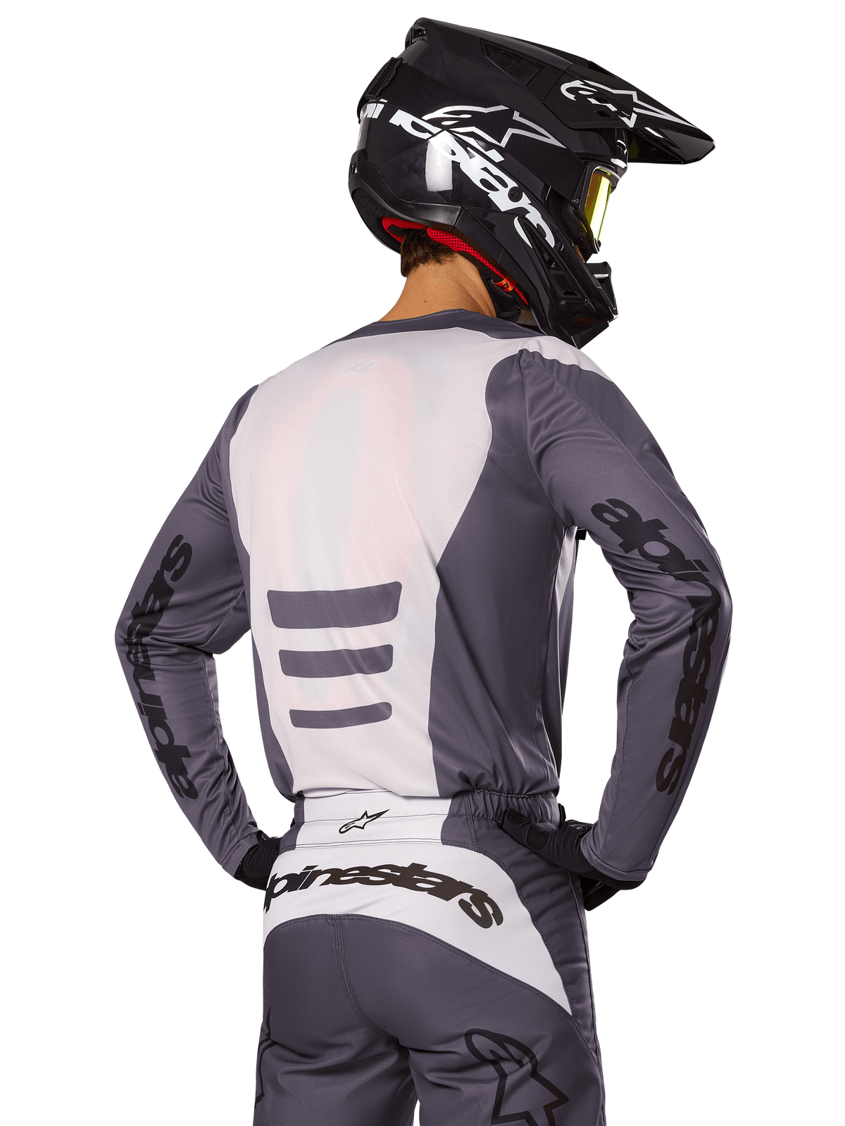 Motocross-Fahrer von hinten in Alpinestars 2025 Fluid Haul Gear Set, grau-weißes Trikot und Hose, schwarzer Helm mit weißen Grafiken, gelbe Brille, abgestimmtes Motocross-Rennoutfit