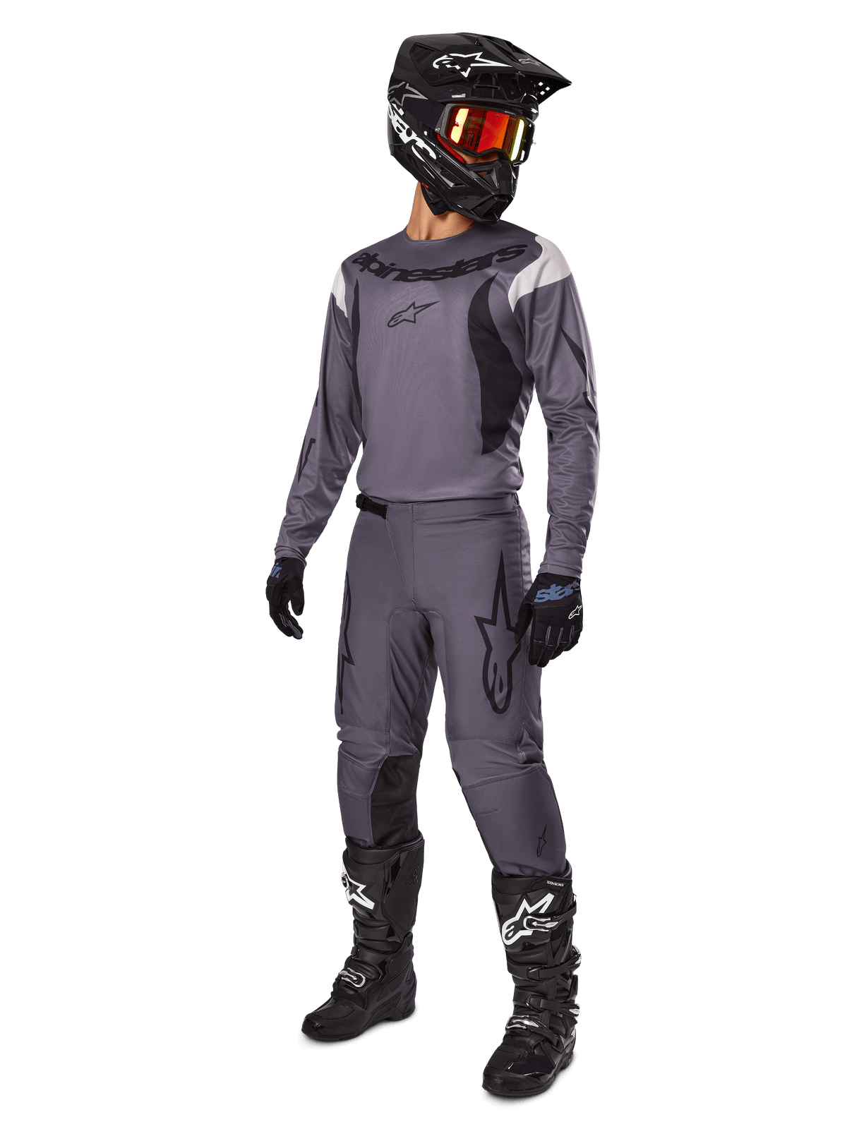 Motocross-Fahrer im Alpinestars 2025 Fluid Haul Ausrüstungsset in Grau, inklusive grauem Jersey und Hose mit schwarzen Akzenten, schwarzem Helm mit rötlicher Brille, schwarzen Handschuhen und schwarzen Stiefeln mit weißen Logos, komplettes Offroad-Rennoutfit