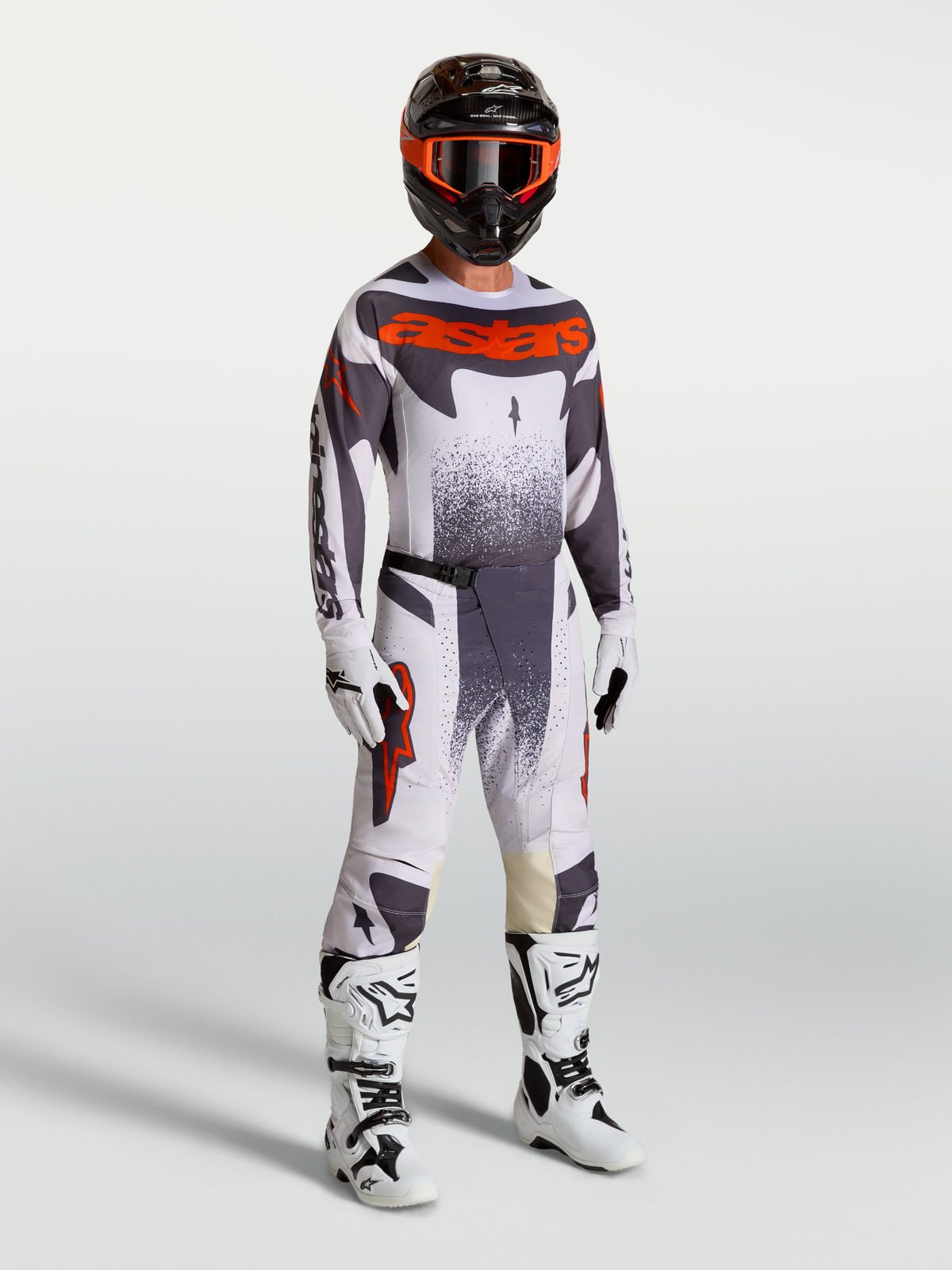 Alpinestars Techstar Swan Trikot und Gear Set am Model, Herren-Motocross-Outfit in Helllila, Grau und fluoreszierendem Rot.