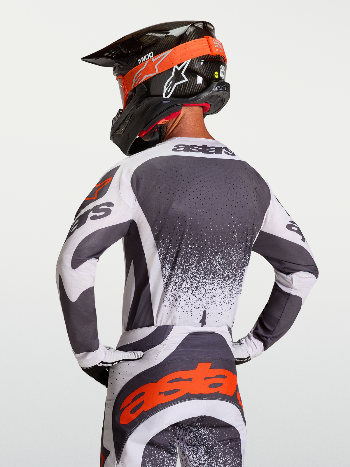Alpinestars Techstar Swan Trikot, athletisches Motocross-Jersey in Dunkelgrau und Weiß mit roten Details, am Fahrer in Rückenansicht gezeigt.