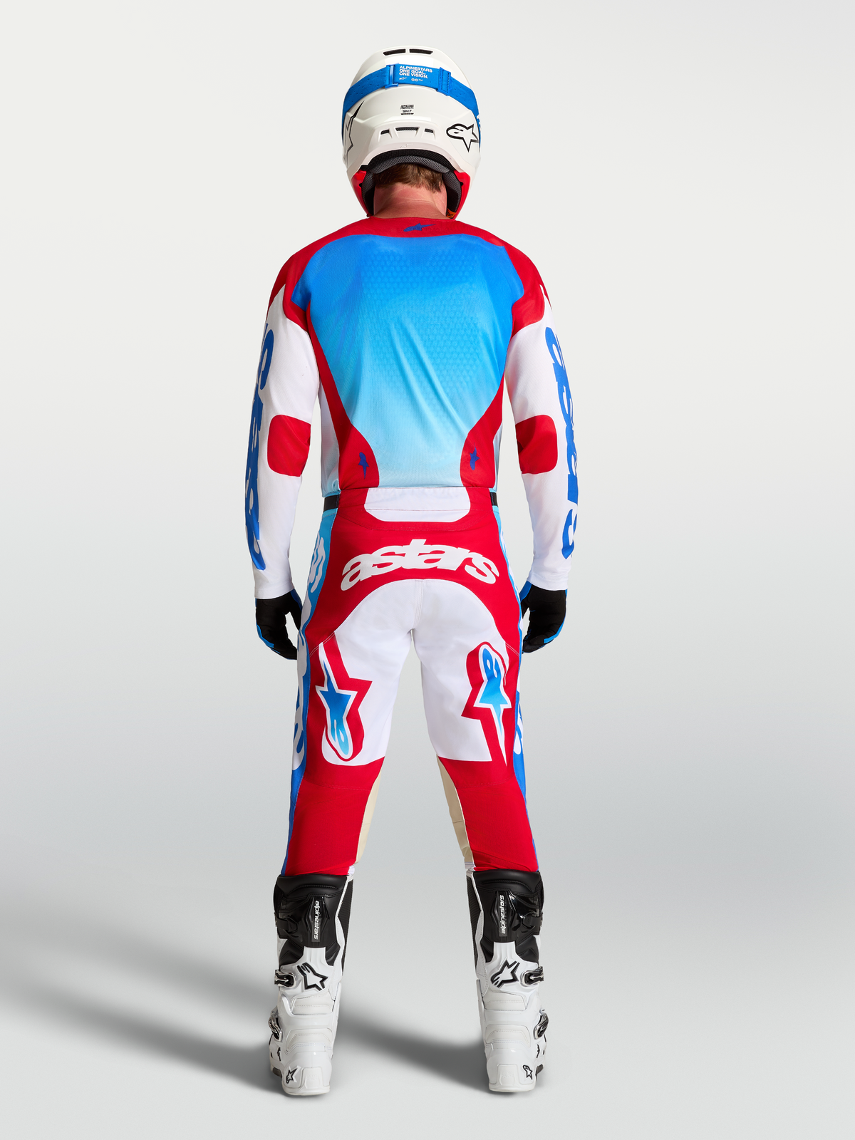 Alpinestars Racer Hose Hunt und Racer Hunt Gear Set, Motocross-Ausrüstung in Rot, Weiß und Blau, Rückansicht am Model mit Helm und Motorradstiefeln.