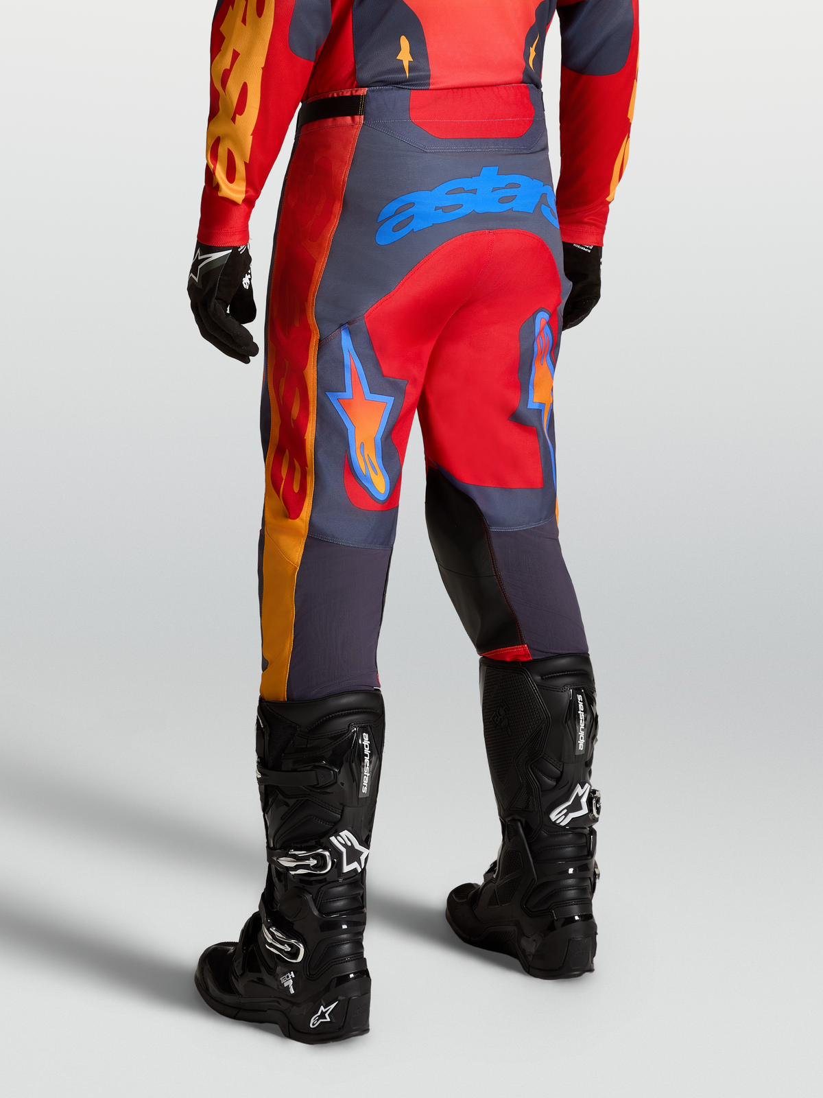 Alpinestars Racer Hunt Hose, Motocross-Performance-Hose in Rot und Grau, Rückansicht in Fahrposition mit schwarzen Tech 7 Stiefeln.
