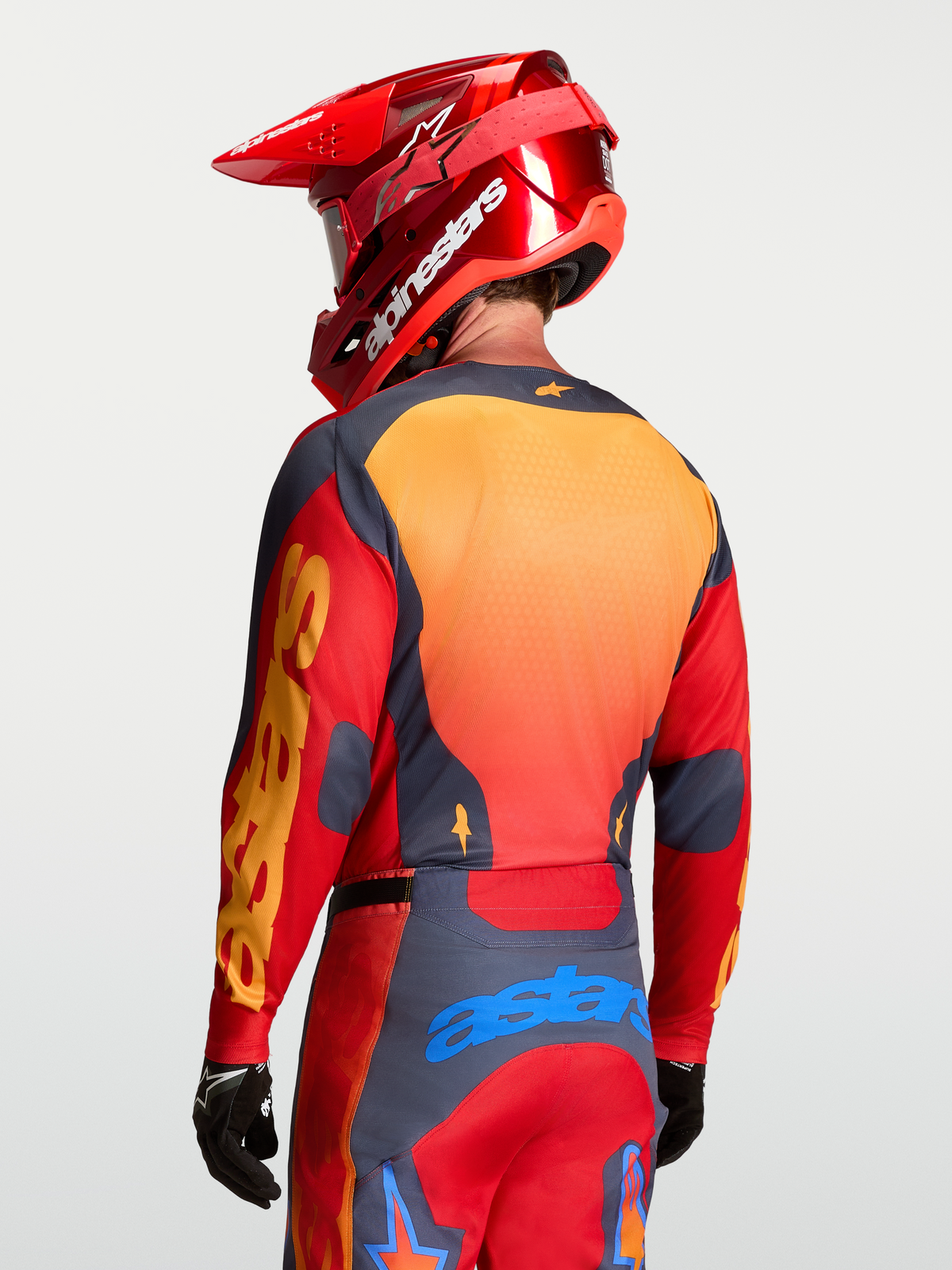 Alpinestars Racer Hunt Trikot, Herren-Motocross-Oberteil, Rot, Grau und Orange, atmungsaktives und feuchtigkeitsableitendes Mesh-Gewebe, Rückansicht mit Helm.
