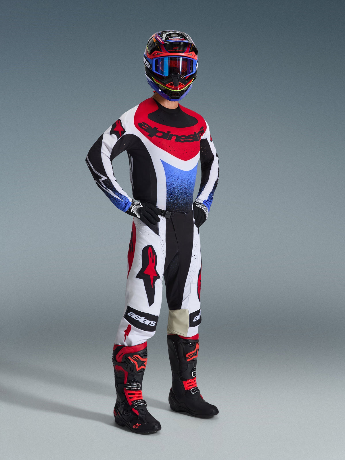 Motocross rider wearing the 2026 Techstar Knif Jersey in Black, White, and Red with blue accents, paired with matching white and red pants, black and red boots, and a helmet with blue goggles, complete off-road racing kit