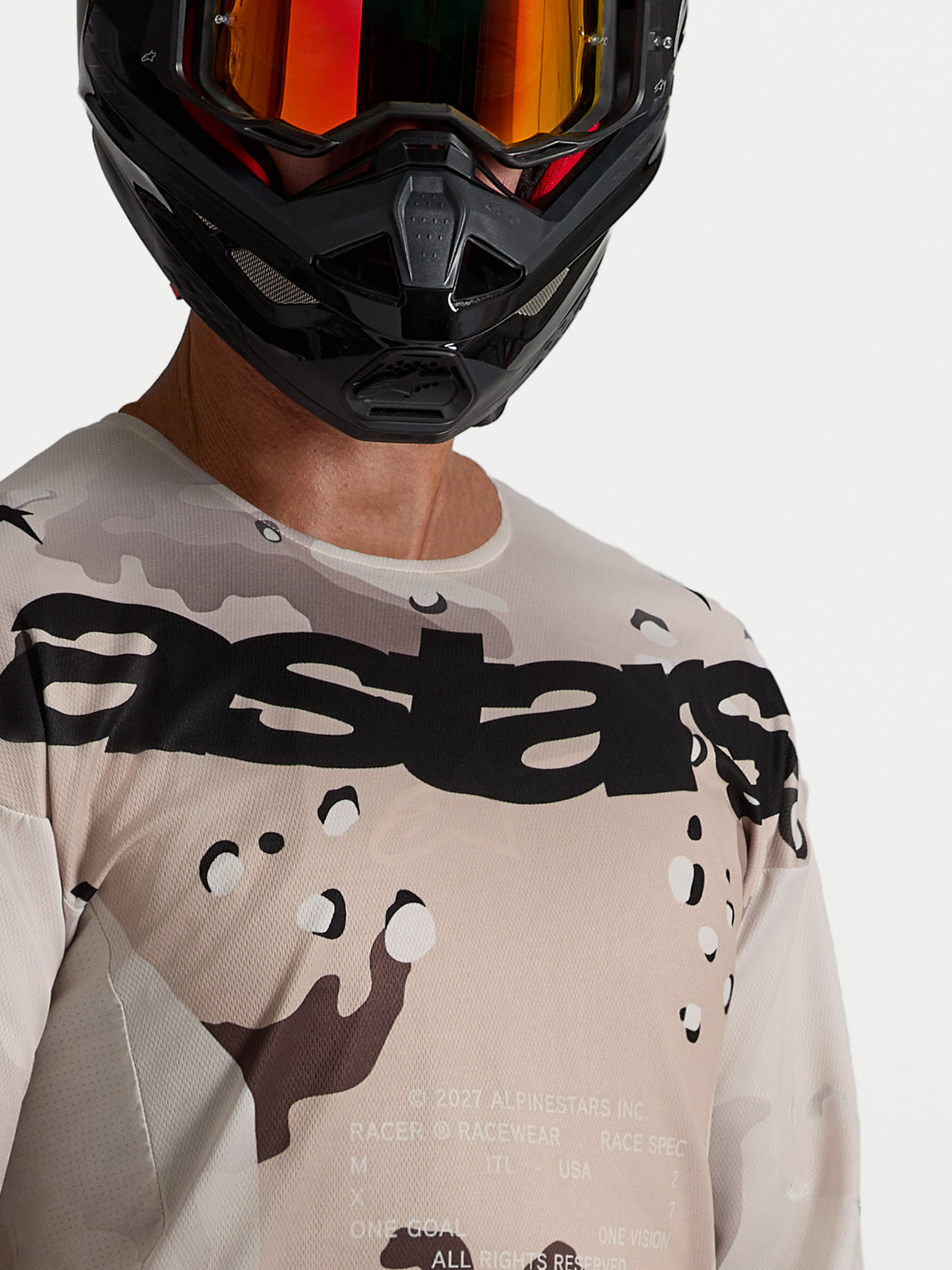 Alpinestars Racer Lone Trikot, Herren-Motocross-Trikot, Desert-Camo und Schwarz, leichtes Polygewebe, Nahaufnahme am Model mit Helm.
