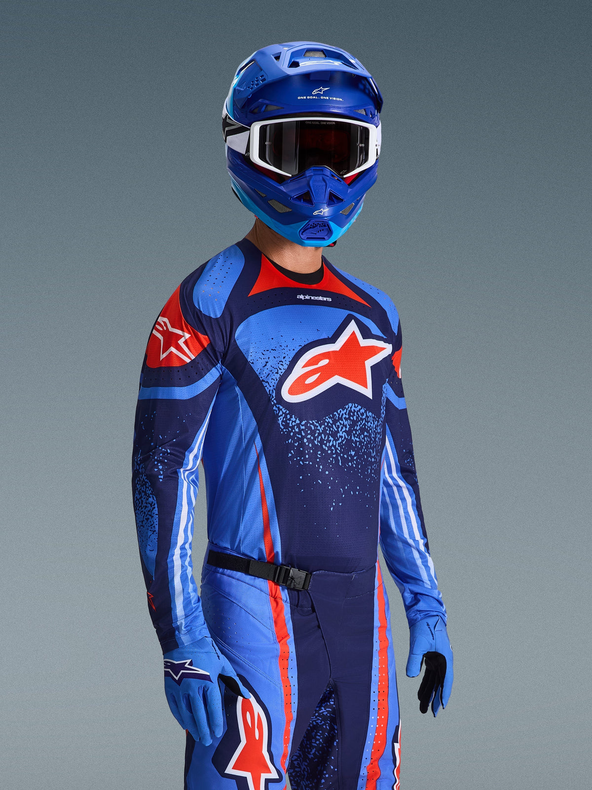 Alpinestars 2026 Techstar Nomur Gear Set, Motocross Jersey and Pants in Dark Navy, Orange, and UCLA Blue, worn by a rider with matching blue helmet and gloves, featuring bold logo graphics and athletic race fit.