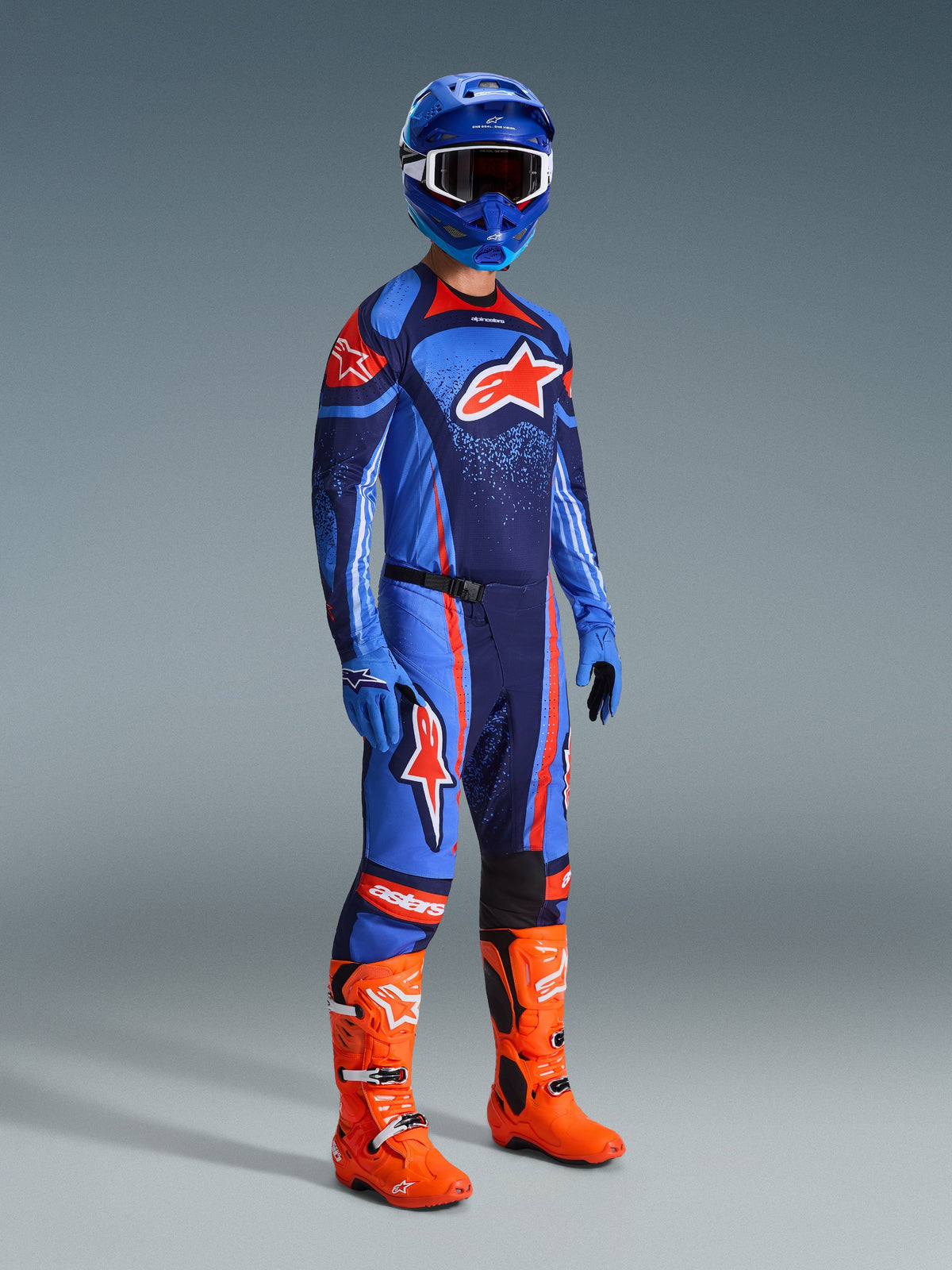 Motocross rider wearing the 2026 Techstar Nomur Gear Set, Dark Navy jersey with light blue and orange accents, matching pants with orange stripes, blue racing helmet, bright orange boots, and blue gloves, coordinated motocross outfit for off-road performance