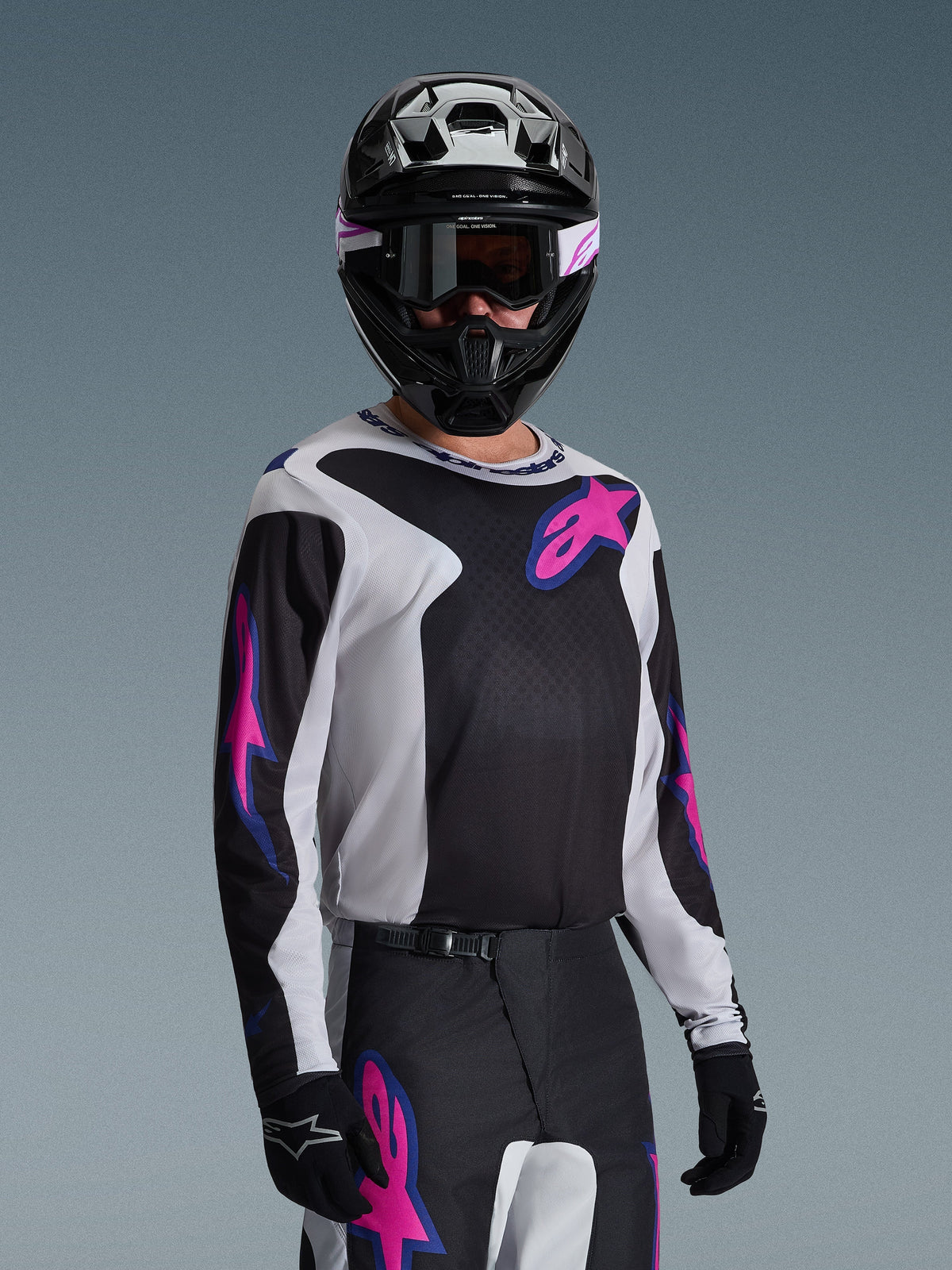 Motocross-Fahrer im Alpinestars 2026 Fluid Grid Jersey in Schwarz, Hellgrau und Lila, mit großen pinkfarbenen und lila Stern-Logos, passender Hose, schwarzem Helm und Goggle, komplettes Offroad-Rennausrüstungs-Set