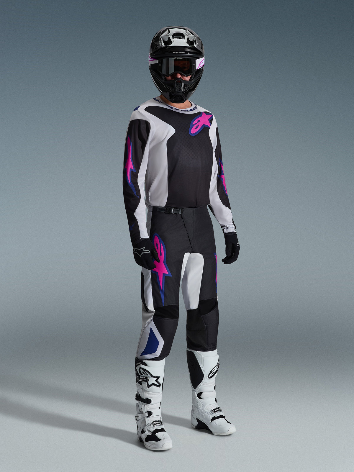 Alpinestars 2026 Fluid Grid Gear Set, motocross rider wearing black and white jersey and pants with pink and blue accents, black helmet, black gloves, and white boots, complete racing ensemble on a gray background