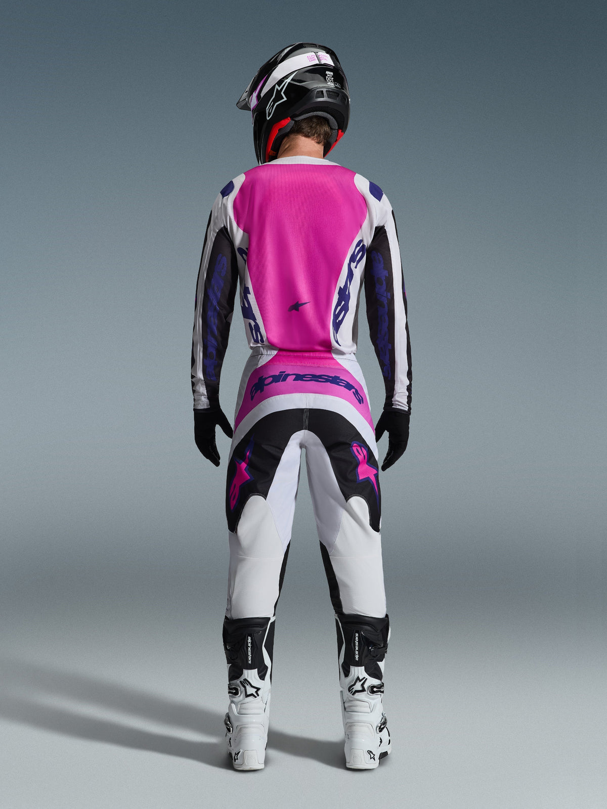 Alpinestars 2026 Fluid Grid Trikot und passende Hose, Motocross-Ausrüstungsset, Pink, Weiß und Lila, Rückansicht zeigt ergonomische sportliche Passform, getragen mit einem schwarzen Helm und weißen Stiefeln, entwickelt für Offroad-Performance.