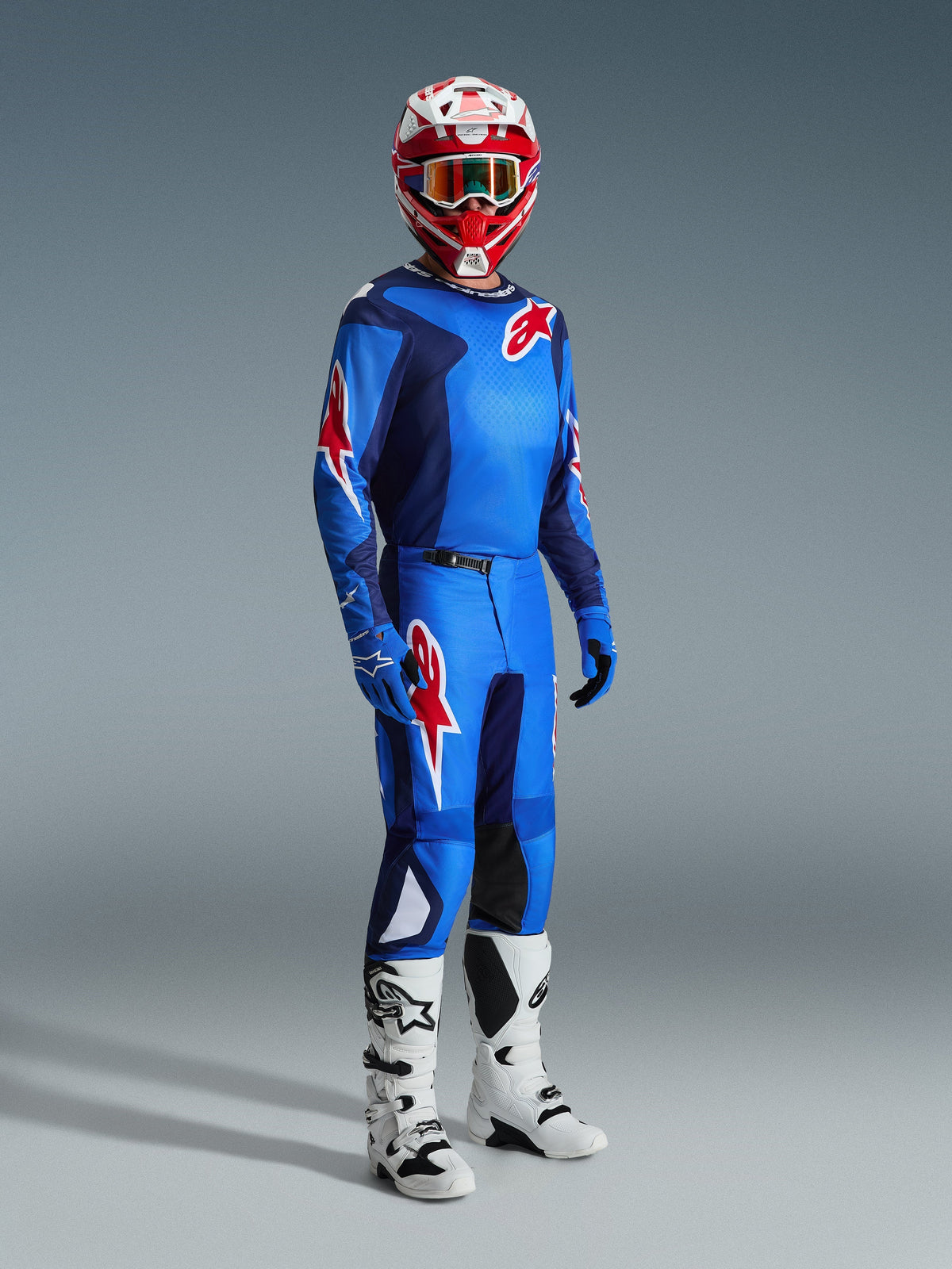 Motocross-Fahrer im Alpinestars 2026 Fluid Grid Trikot in Blau-Rot, kombiniert mit der passenden Motocross-Hose, weiß-schwarzen Stiefeln und einem rot-weißen Helm, professionelles Ausrüstungsset für Offroad-Performance.