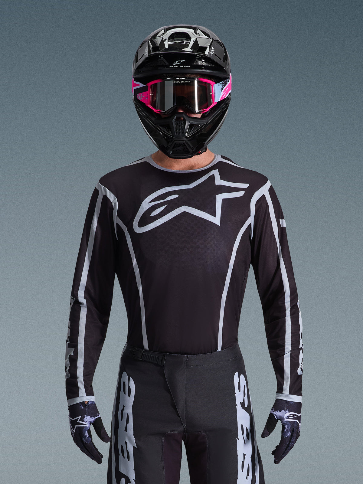 Alpinestars 2026 Fluid Apex Ausrüstungsset, Motocross-Trikot und -Hose in Schwarz und Weiß, mit großem Brustlogo und geometrischen Linien-Designs, getragen mit einem schwarzen Helm und einer pinkfarbenen Brille, Performance-Ausrüstung für Offroad-Motocross-Rennen.