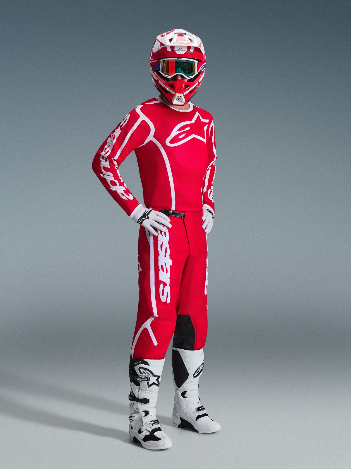 Motocross rider wearing complete Alpinestars racing gear, featuring the 2026 Fluid Apex Jersey in Red and White, matching red pants with white branding, red and white helmet with goggles, white and black motocross boots, and white gloves, professional studio shot of off-road gear.