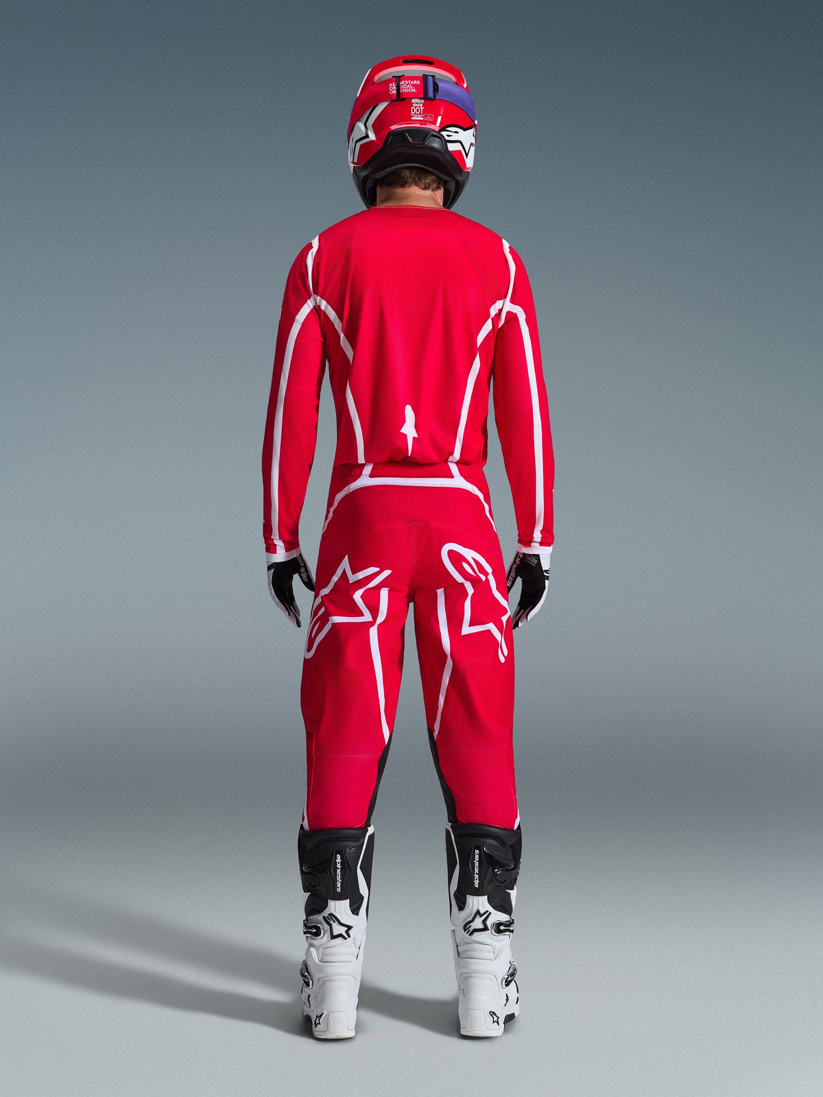 Motocross rider viewed from behind wearing the Alpinestars 2026 Fluid Apex Jersey in Red and White, matching red pants with prominent white star logos, a red helmet, white and black motocross boots, and black and white gloves, complete kit for off-road racing