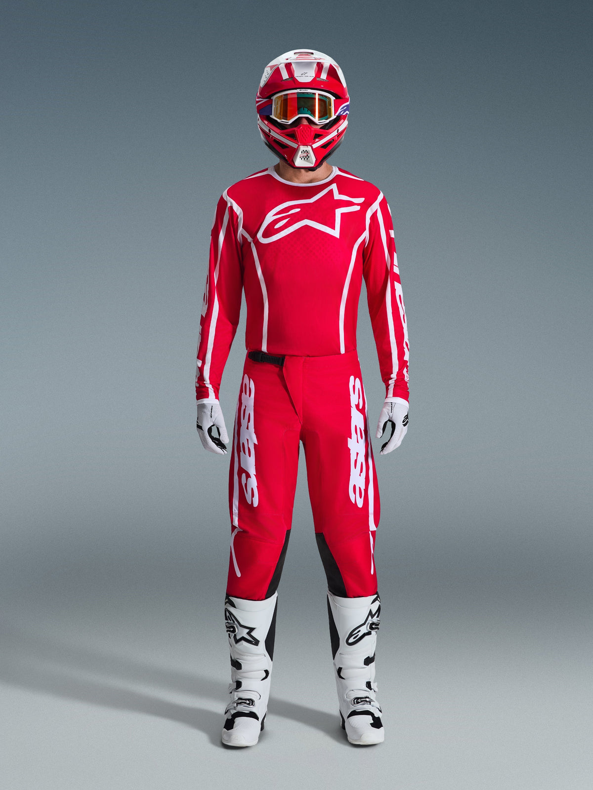 Motocross rider wearing complete 2026 Fluid Apex racing gear, Red jersey with white Alpinestars logo and sleeve branding, matching red pants with white accents and black panels, red and white helmet with mirrored goggles, white and black boots, and white and black gloves, professional gear set for off-road performance.