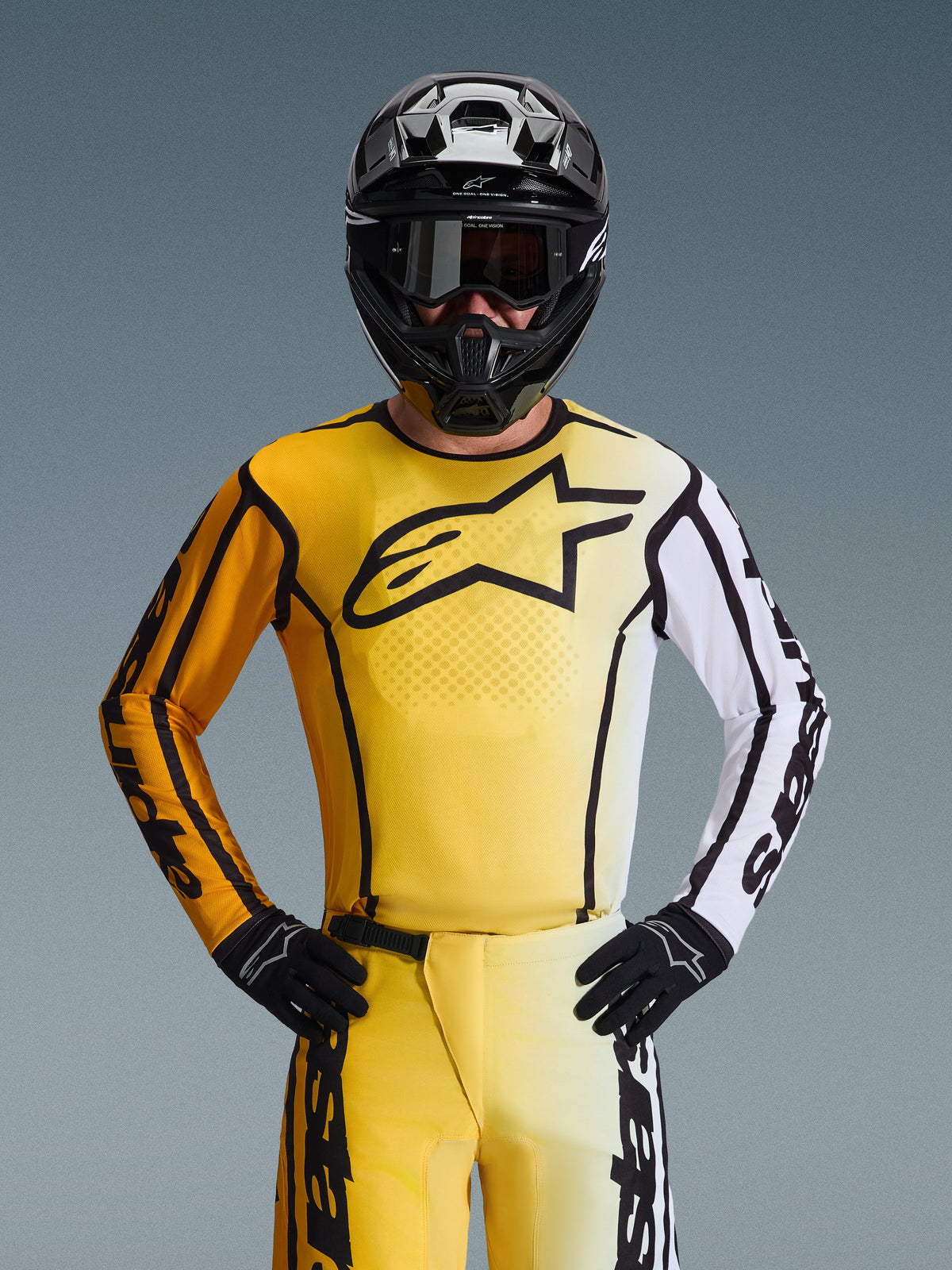 Motocross-Fahrer im Alpinestars 2026 Fluid Apex Gear Set, gelb-weißes Jersey mit großem schwarzem Stern-Logo, passende gelb-weiße Hose, schwarzer Helm mit schwarzer Goggle und schwarze Handschuhe, koordiniertes Outfit für den Offroad-Rennsport