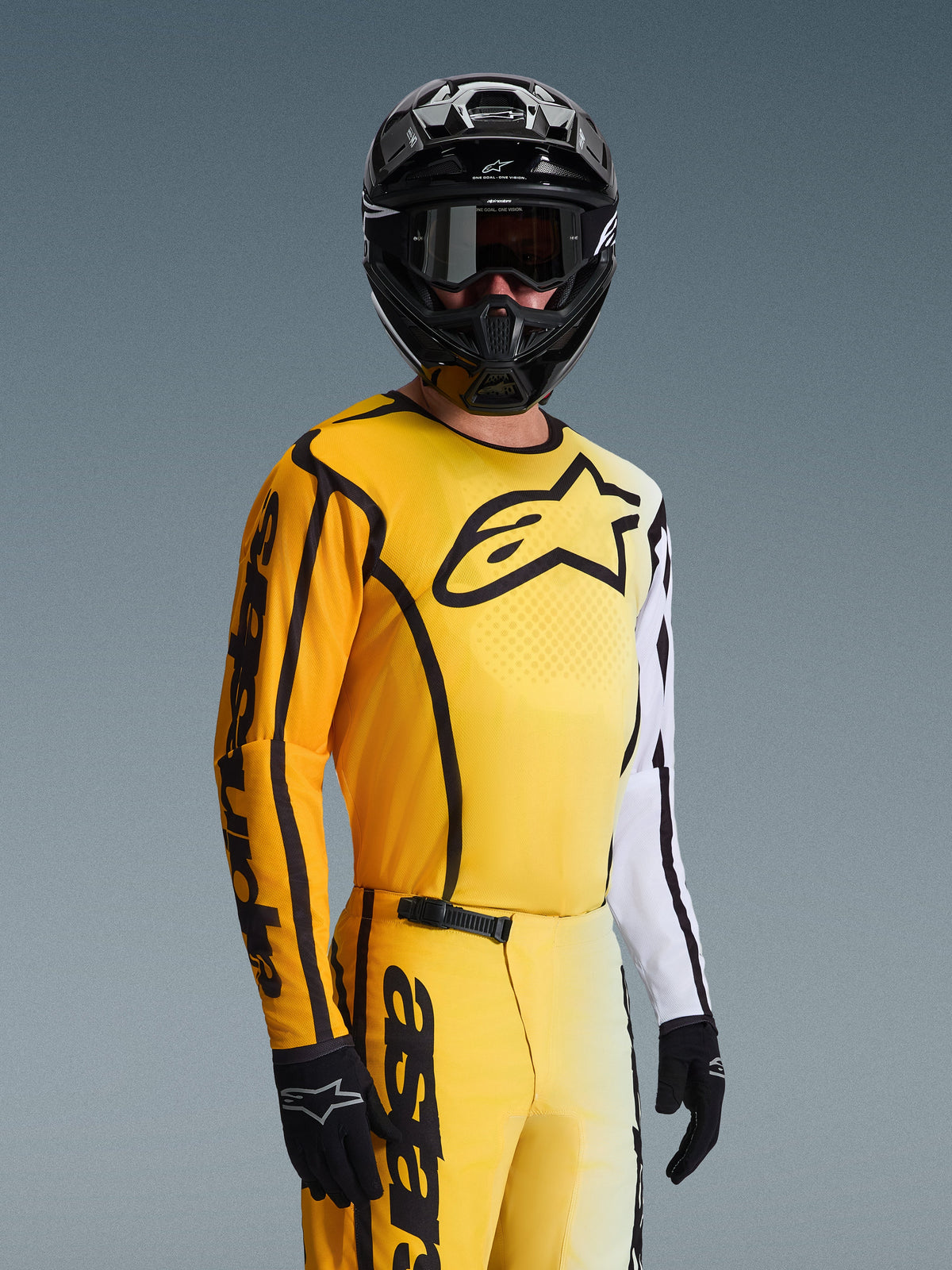 Motocross-Fahrer im Alpinestars 2026 Fluid Apex Gear Set, gelb-weißes Trikot mit schwarzem Stern-Logo und Akzenten, passende gelbe Hose, schwarzer Helm mit schwarzer Brille und schwarze Handschuhe, abgestimmtes Outfit für Offroad-Rennsport