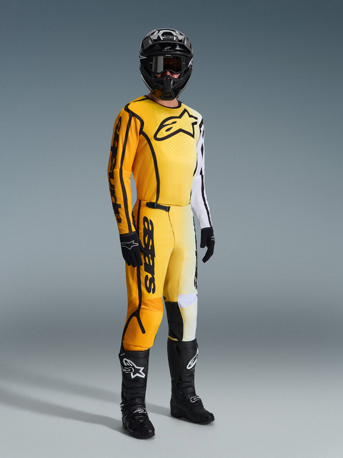 Alpinestars 2026 Fluid Apex Ausrüstungsset, Motocross-Fahrer in gelber, weißer und schwarzer Rennausrüstung, Trikot mit großem Brustlogo und weißem Ärmel, passende Hose mit auffälligem Branding, schwarzer Helm, Handschuhe und Stiefel, abgestimmtes Outfit für den Offroad-Rennsport