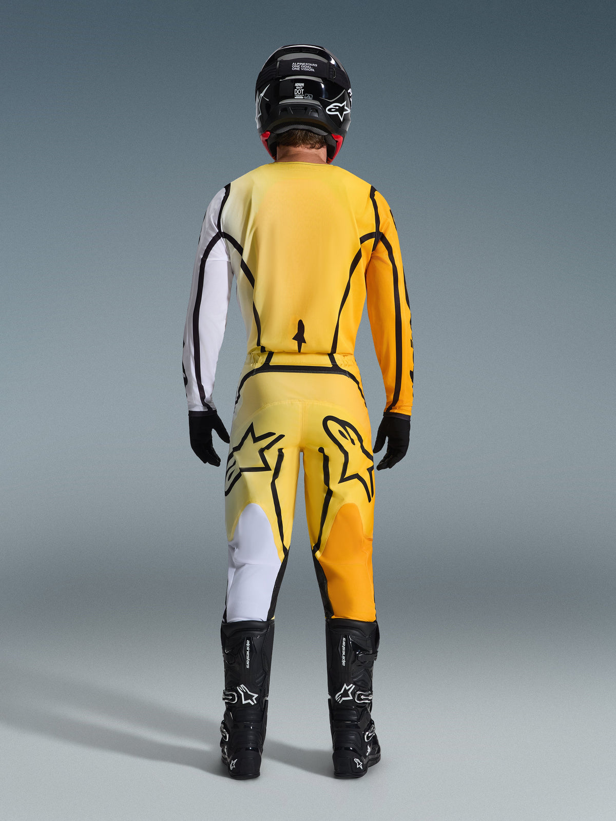 Motocross-Fahrer in der Rückansicht mit dem Alpinestars 2026 Fluid Apex Gear Set, gelbes Trikot mit weißem Ärmel und schwarzen Akzenten, passende gelbe Hose mit großen schwarzen Alpinestars-Logos auf der Rückseite, schwarzer Helm, schwarze Handschuhe und schwarze Stiefel, abgestimmtes Outfit für den Offroad-Rennsport