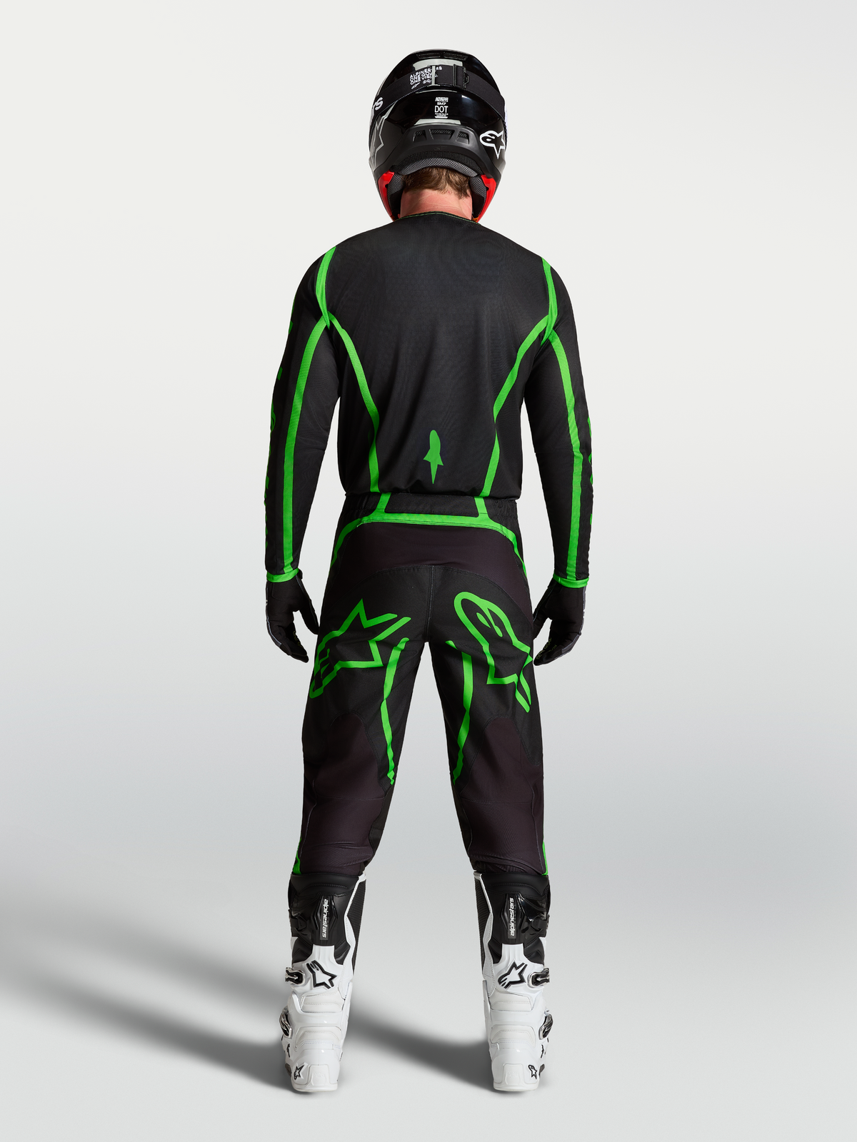 Alpinestars Fluid Apex V2 Trikot, Motocross-Ausrüstung, Schwarz und Leuchtgrün, Rückansicht am Fahrer mit weißen Stiefeln.