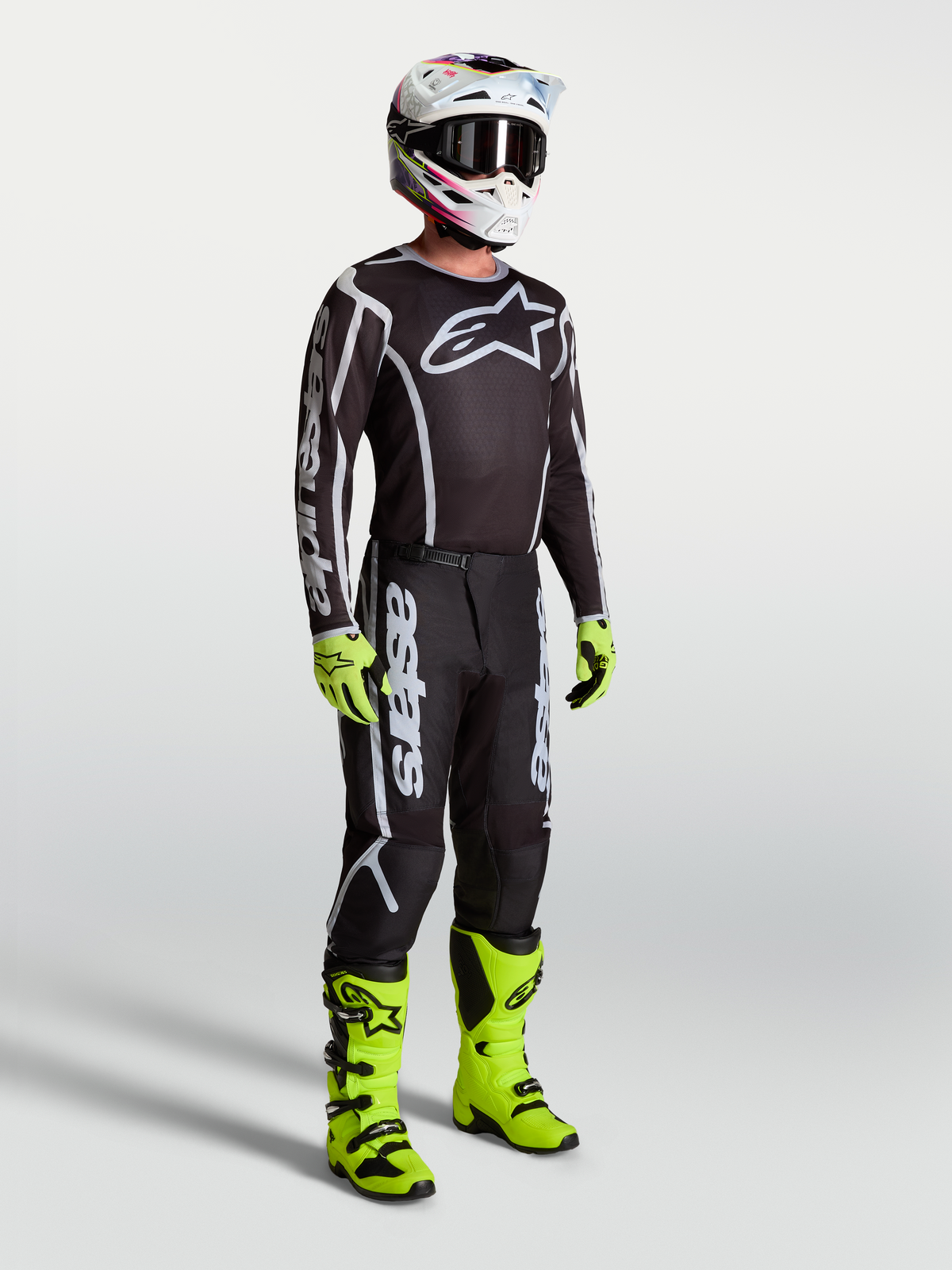 Alpinestars Fluid Apex V2 Trikot, schwarz-silberne Motocross-Bekleidung am Model mit neon-grünen Stiefeln und Handschuhen.