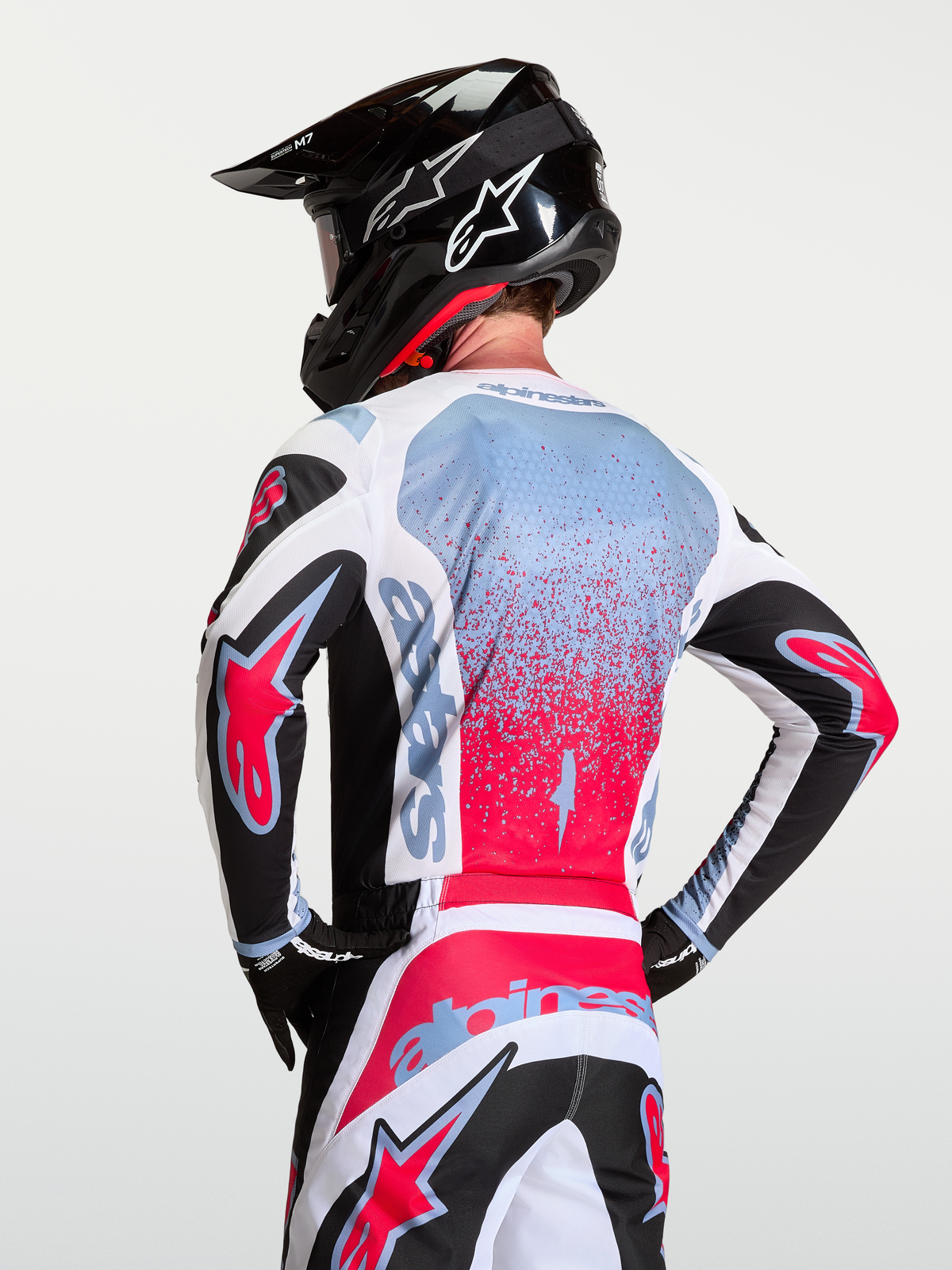 Alpinestars Fluid Drag Trikot, Herren-Motocross-Ausrüstung, Schwarz, Weiß und Rot mit hellblauen Akzenten, atmungsaktives Polygewebe, Rückansicht auf Model mit Helm.