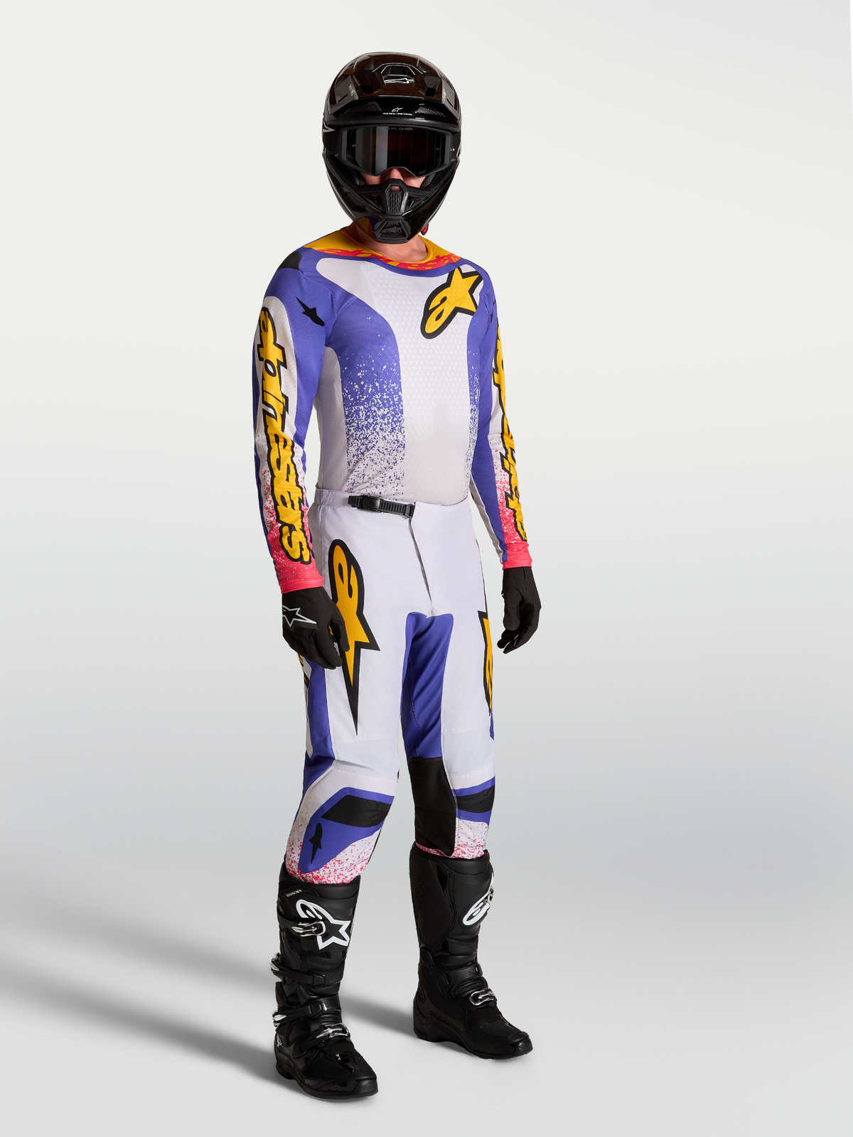 Alpinestars 2027 Fluid Drag Gear Set und Fluid Drag Hose, Herren-Motocross-Bekleidung in Lila, Blau und Gold, am Model.