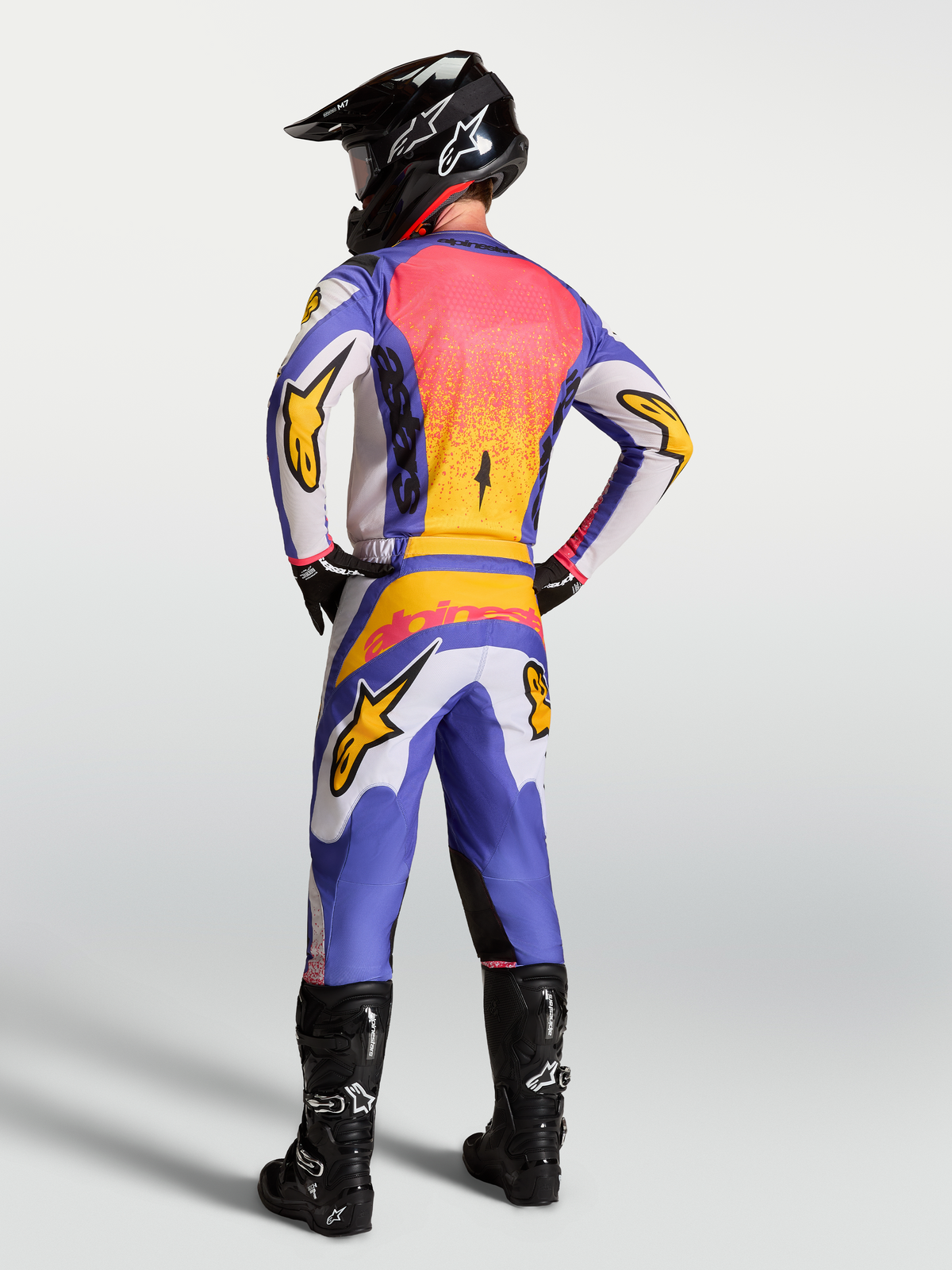 Alpinestars Fluid Drag Trikot in Lila und Blau mit Gold, Rückansicht eines Motocross-Fahrers in voller MX-Ausrüstung.